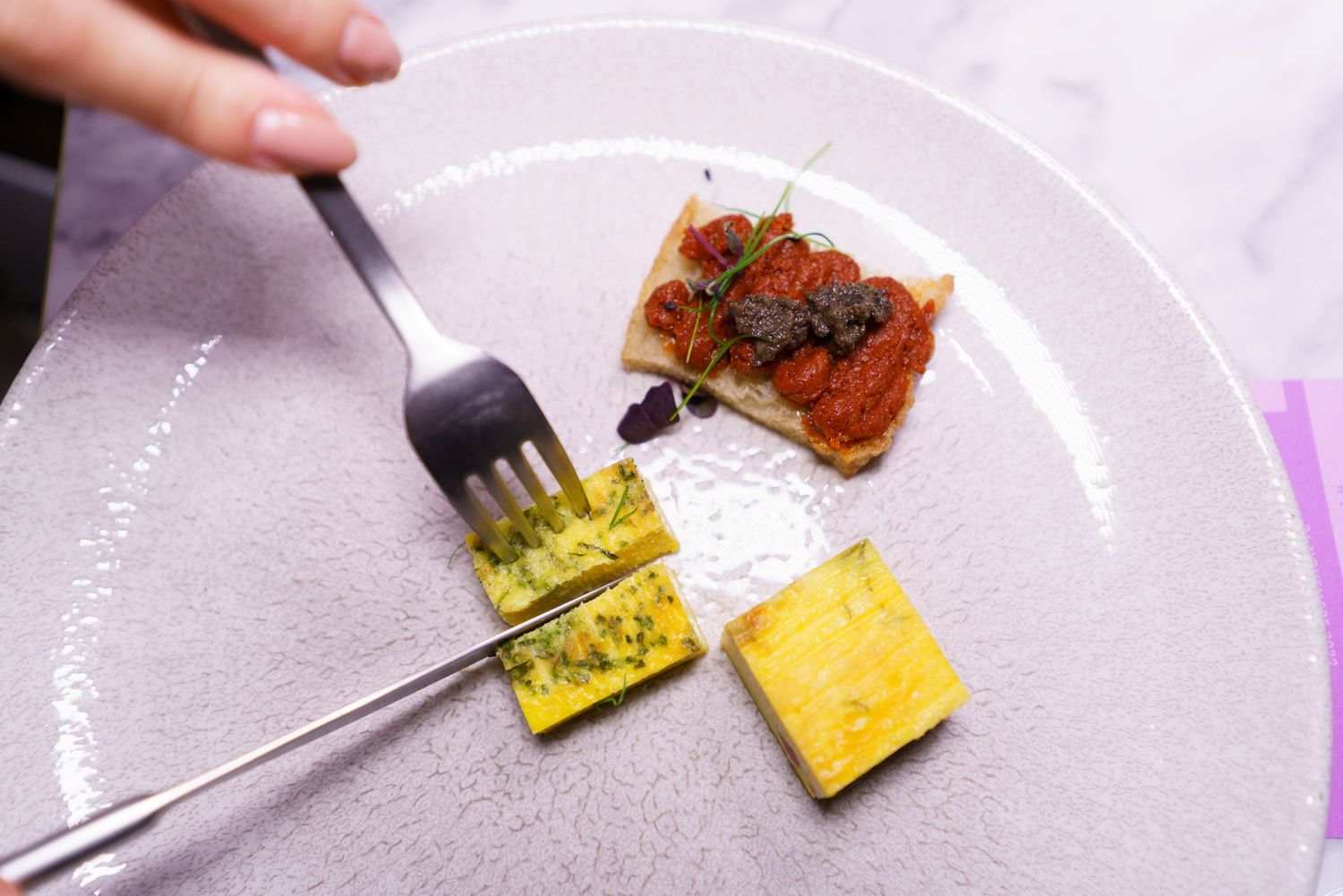 Close-up of an elegant gourmet dish with yellow polenta squares and bruschetta topped with tomatoes on a white plate.