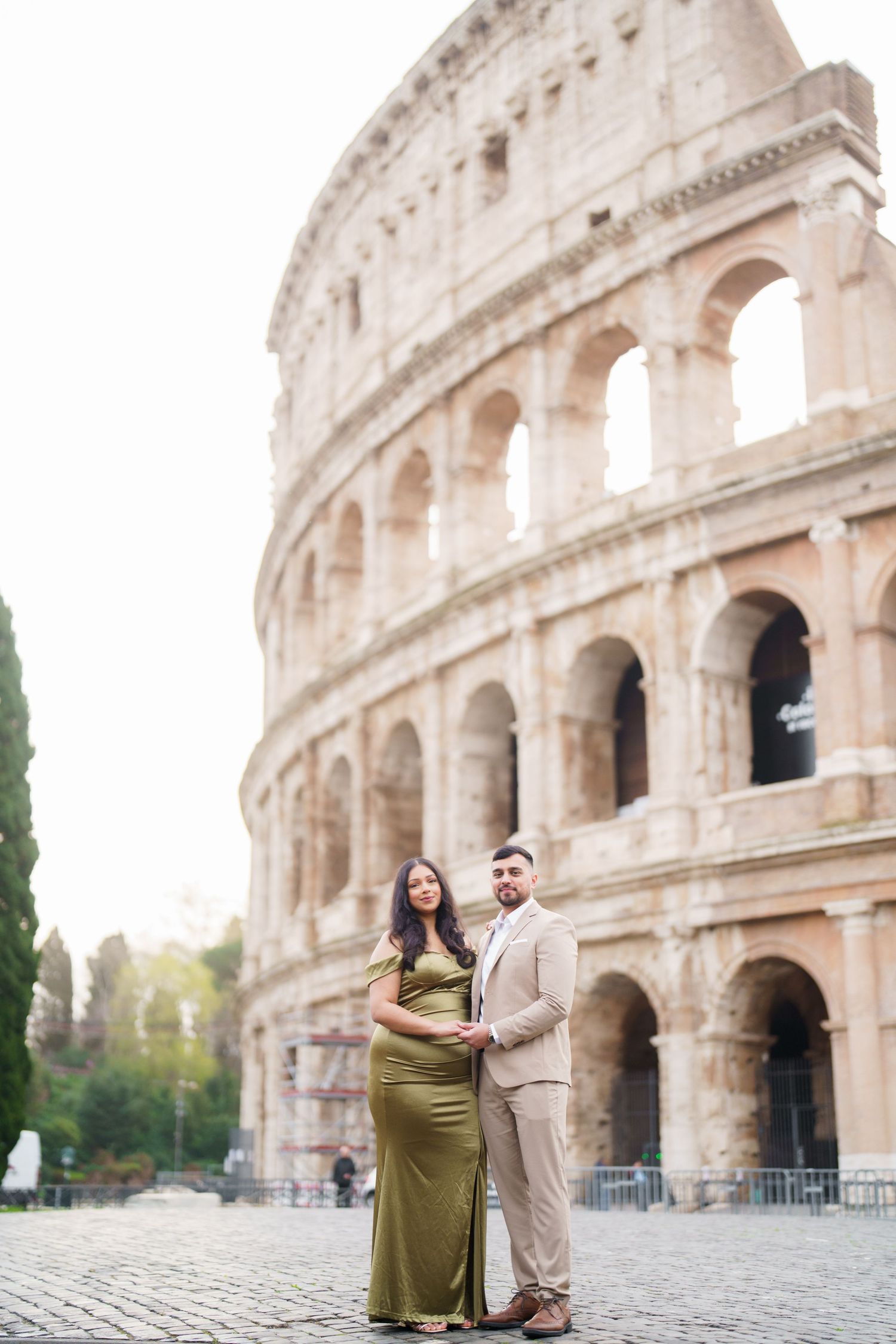 Elegant couple posing in front of the Colosseum in Rome, woman in green gown, man in beige suit.