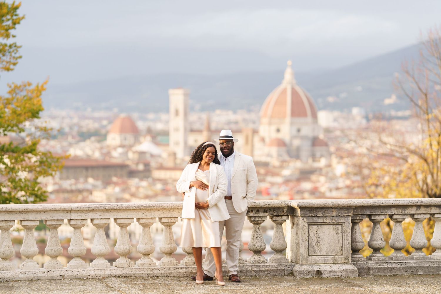 Couple in white attire posing on a terrace with Florence skyline and Duomo cathedral in background.