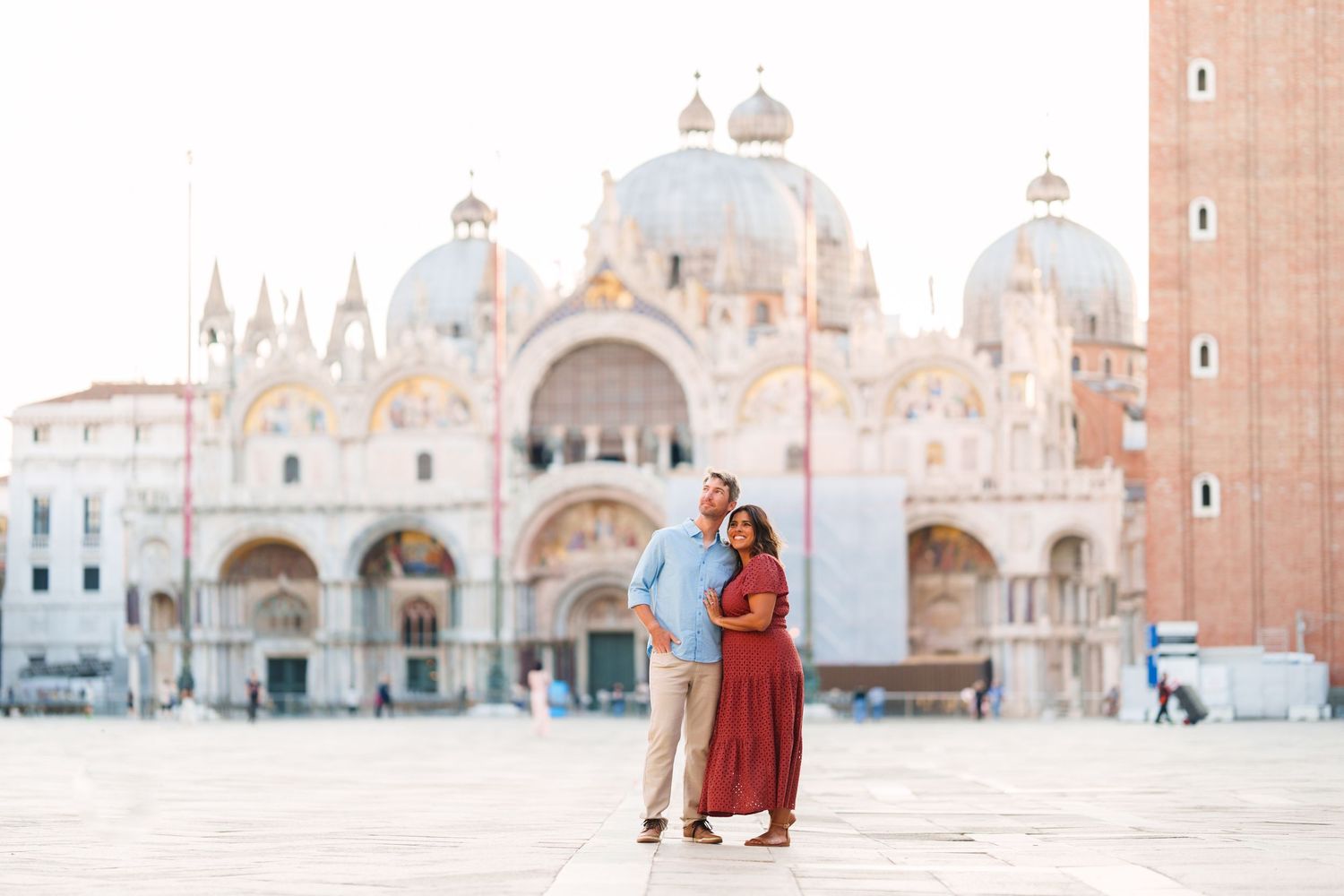 Couple embracing in St. Mark's Square, Venice, with the iconic Basilica di San Marco in the background.