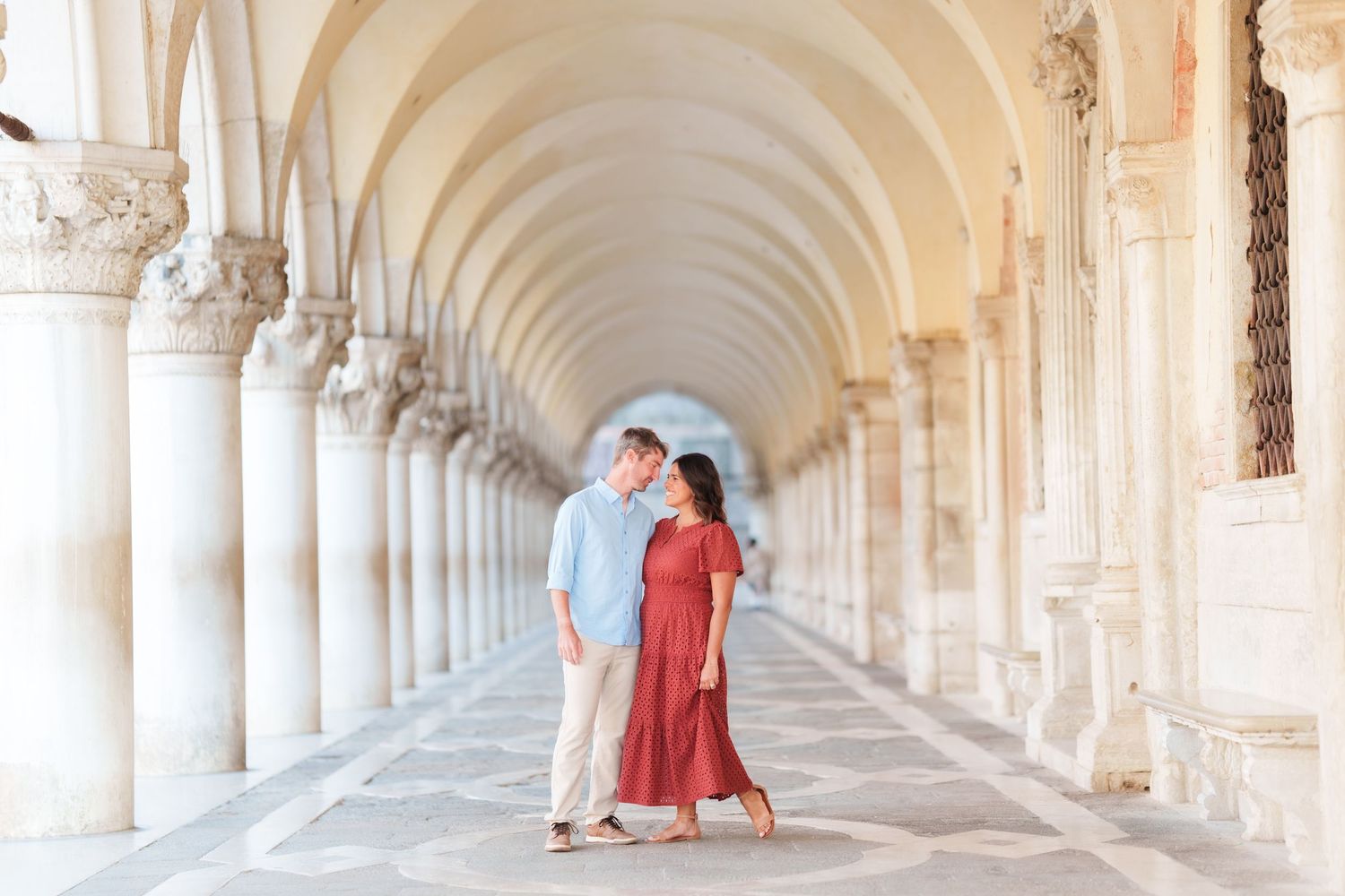 Couple sharing a romantic moment under elegant arched colonnade in Venice, Italy.