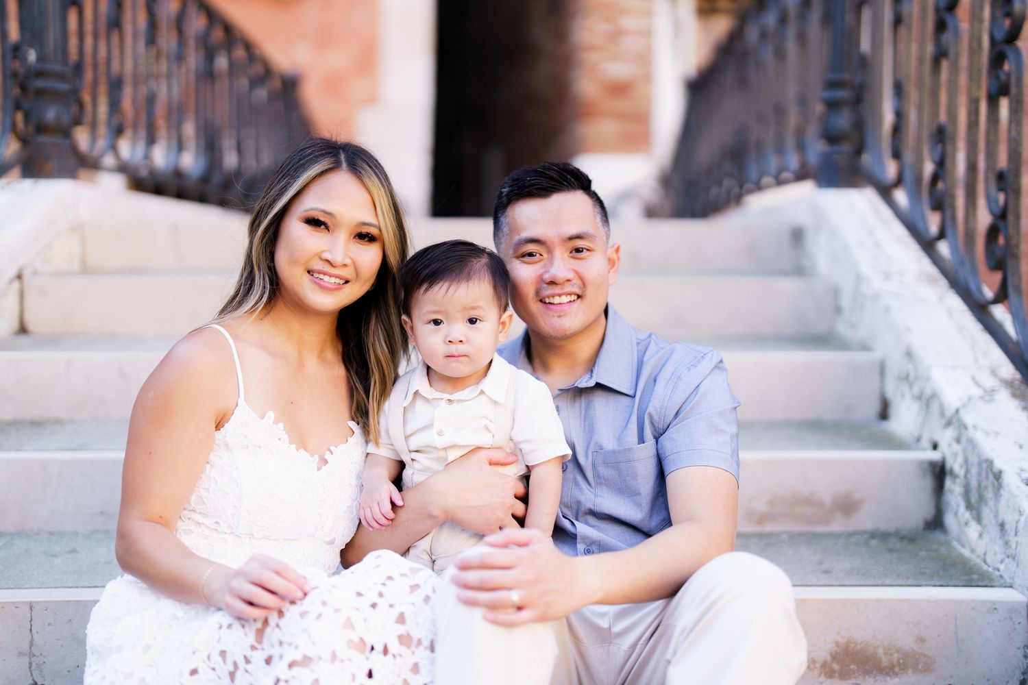 Young family with baby sitting on stone steps, smiling together in a warm outdoor portrait session.