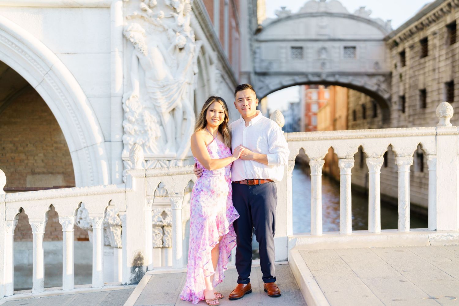 Couple posing together on a bridge in Venice, Italy, with the Bridge of Sighs visible in the background.