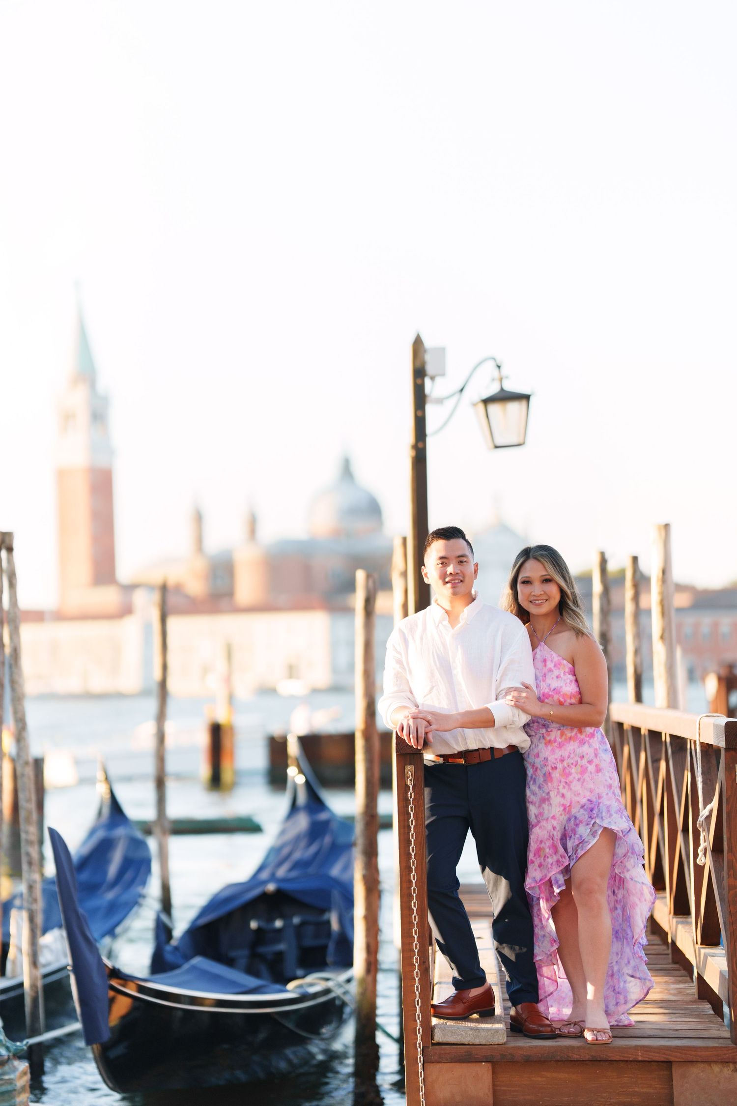 Couple posing on a Venice gondola dock with San Giorgio Maggiore church and gondolas in the background.