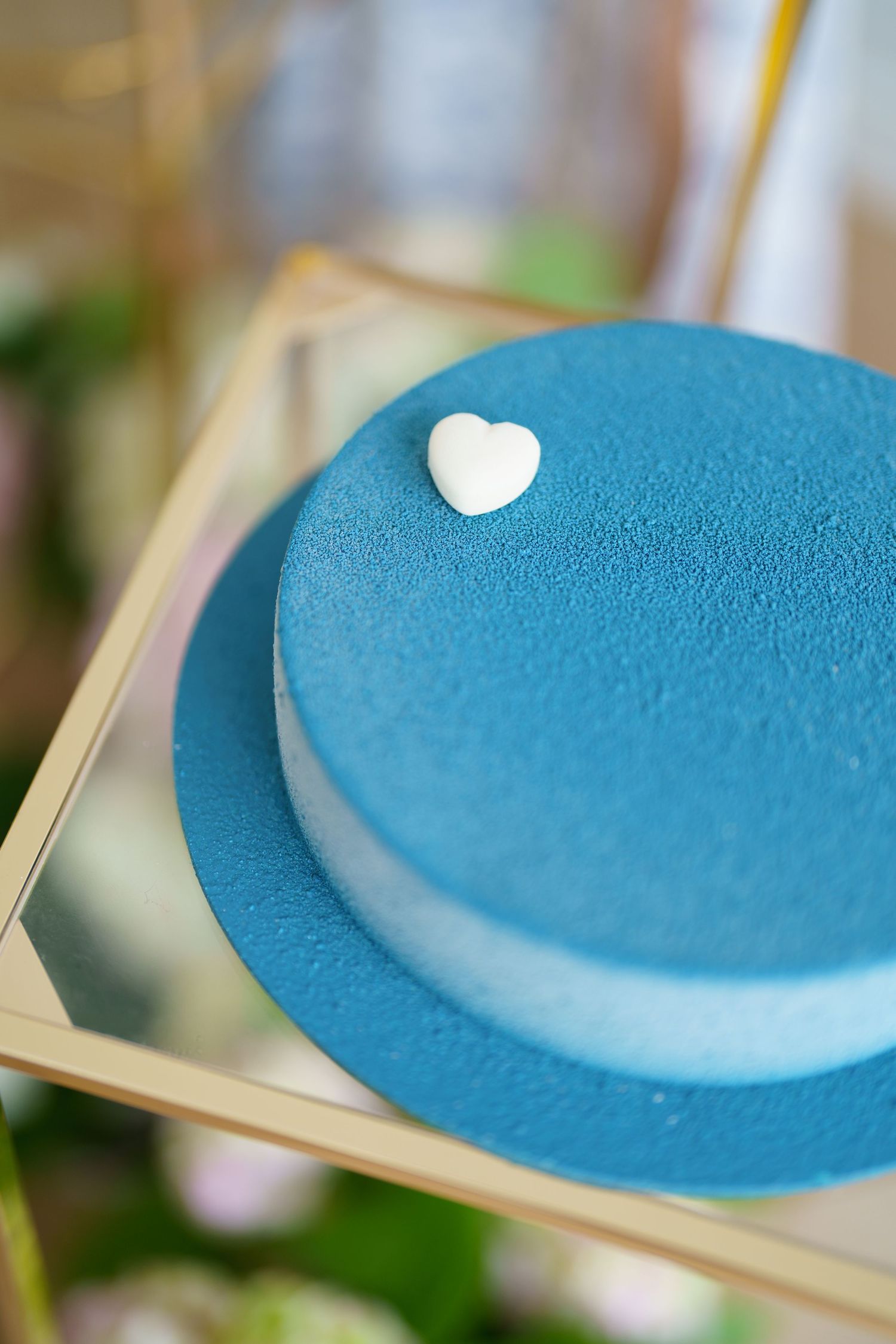 Elegant blue velvet cake with white heart decoration on gold mirrored stand.