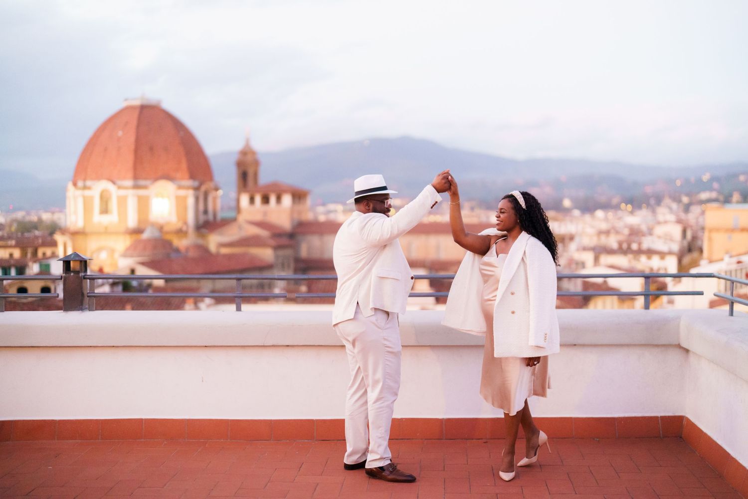 Couple dancing on rooftop terrace in Florence Italy with iconic Duomo cathedral dome and cityscape at dusk.