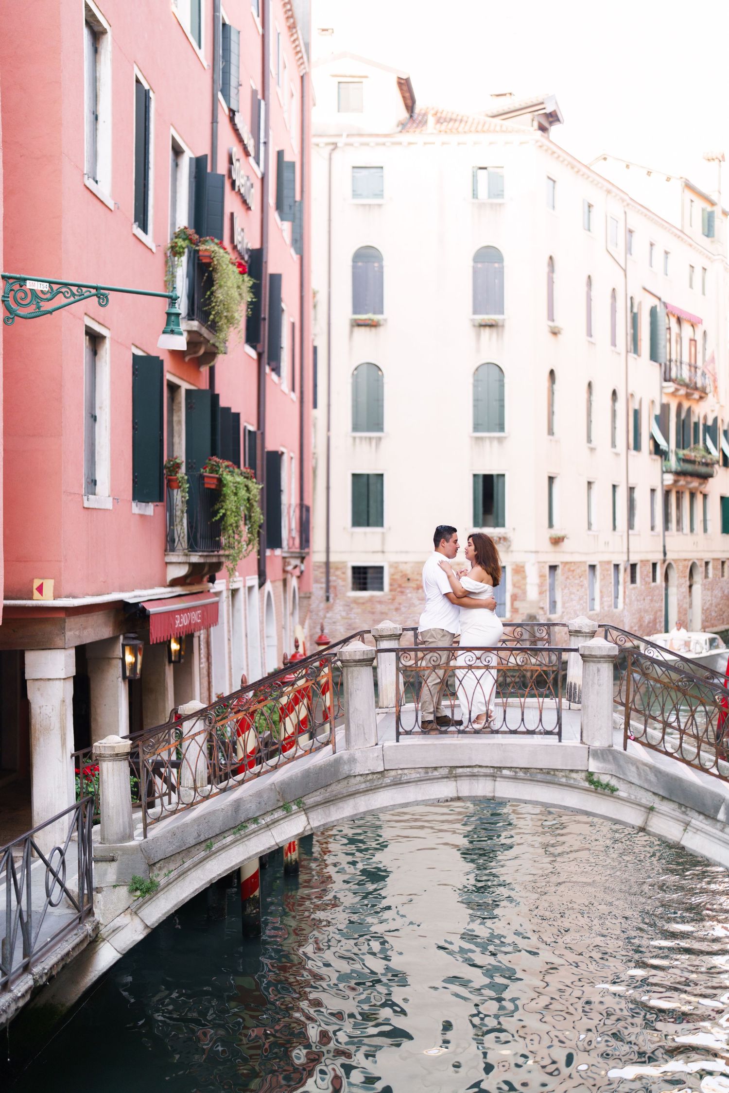 Scenic view of a traditional Venetian canal with pink buildings, ornate bridges and reflective water in Venice, Italy.