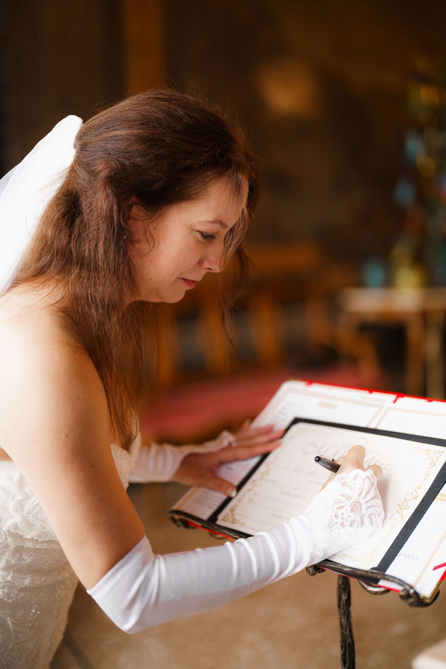 A person in a white top writes in a notebook at a desk in warm lighting.