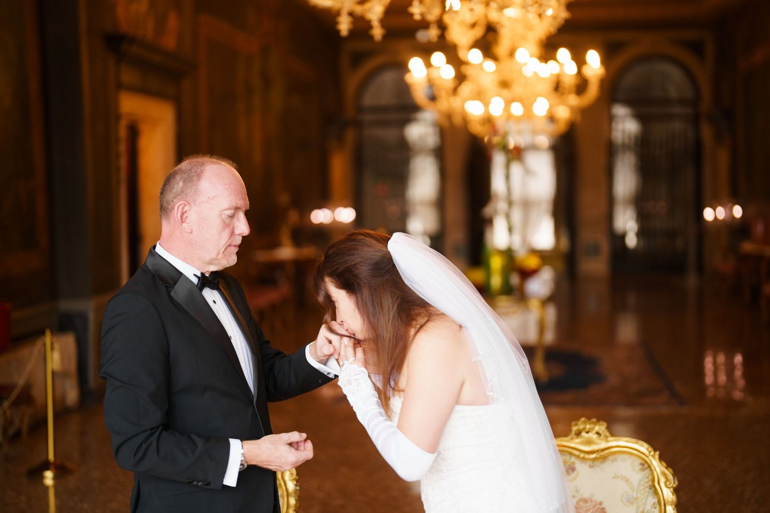 A couple shares their first dance at an elegant wedding reception under glowing chandeliers.