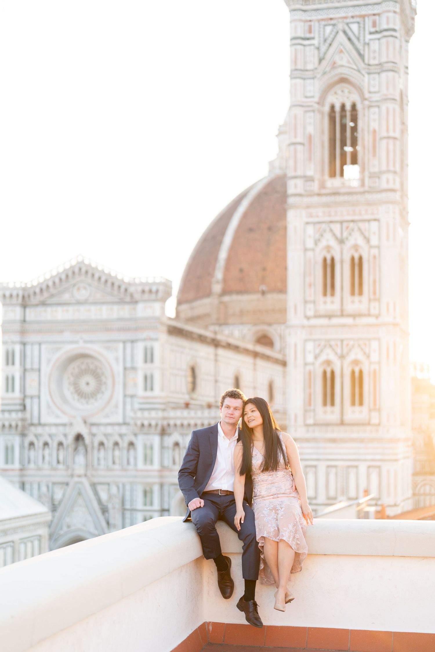 A romantic couple sits on a rooftop terrace overlooking the iconic Florence Cathedral and Duomo at sunset.