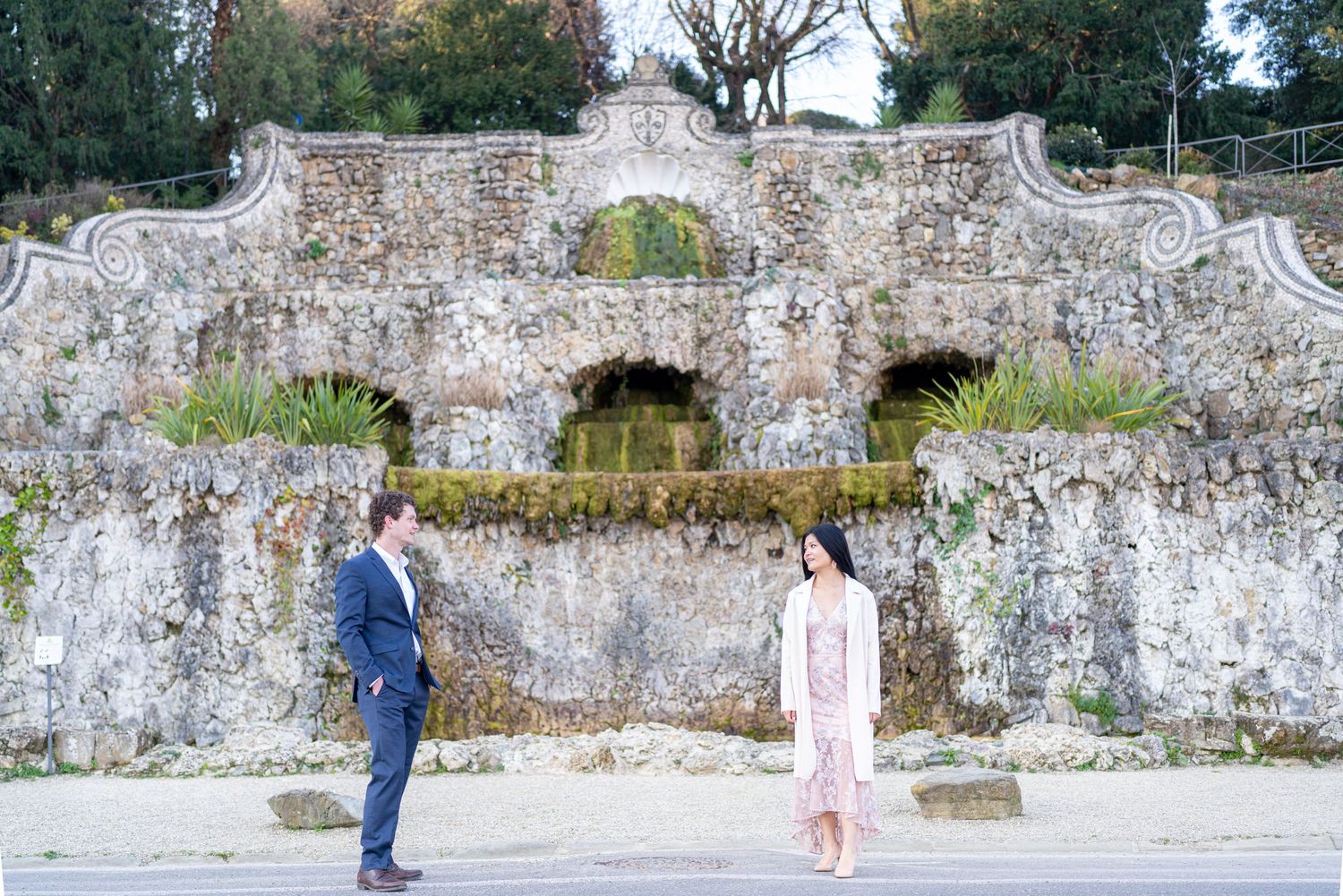 A couple shares a romantic moment against a rustic stone wall in an outdoor garden setting.