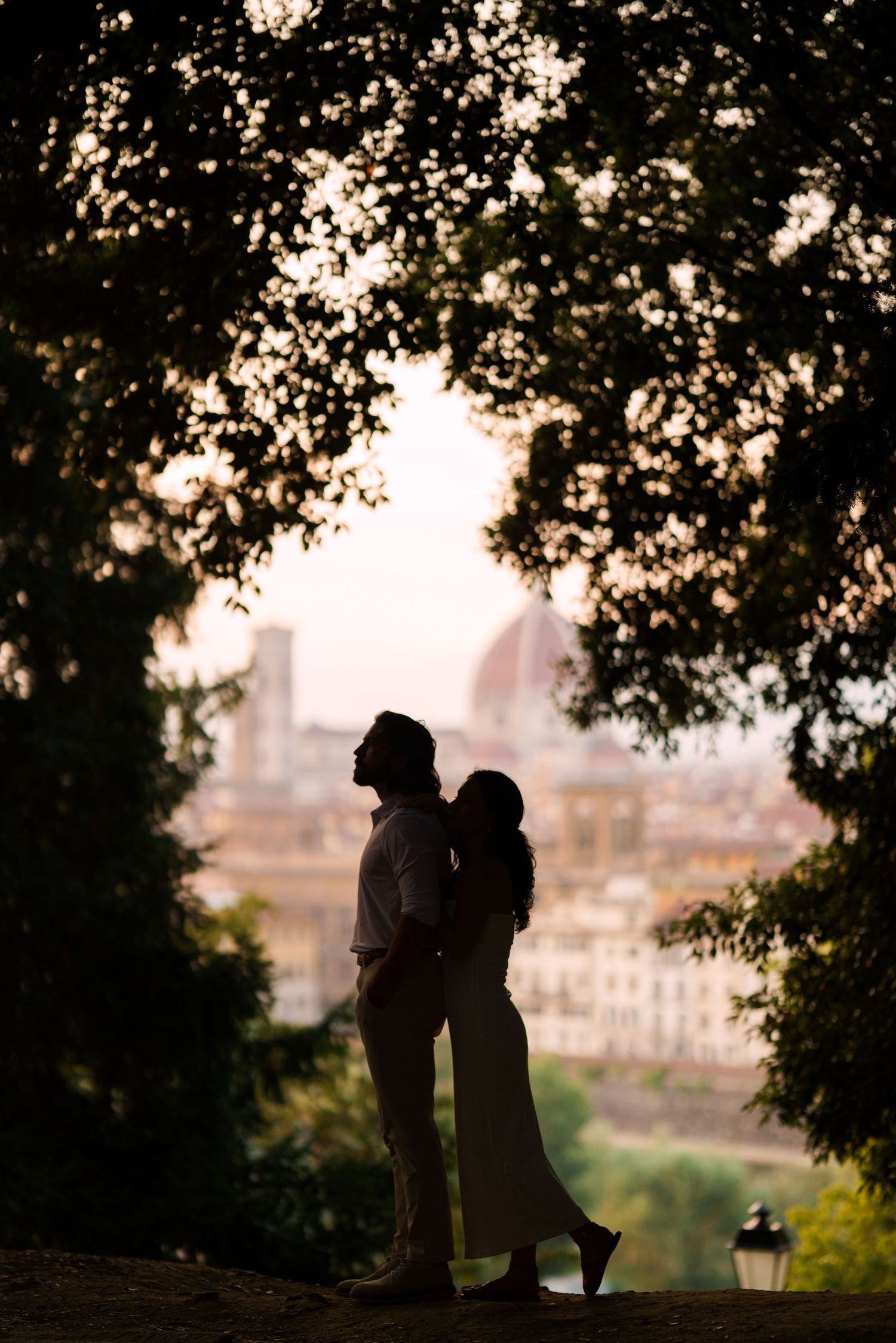 Silhouetted couple stands together at sunset overlooking Florence, Italy with the Duomo cathedral visible in background.