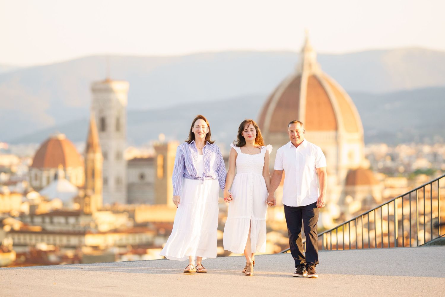 A group in white outfits walks along a Mediterranean coastal promenade with historic buildings in the background.
