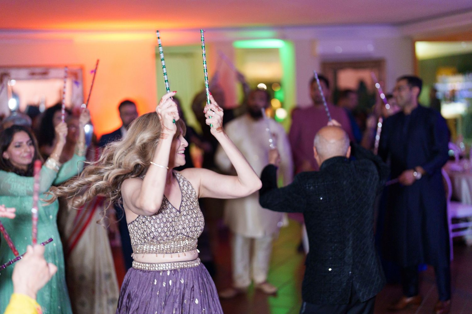 Guests dancing with sparklers at an indoor celebration with colorful lighting.