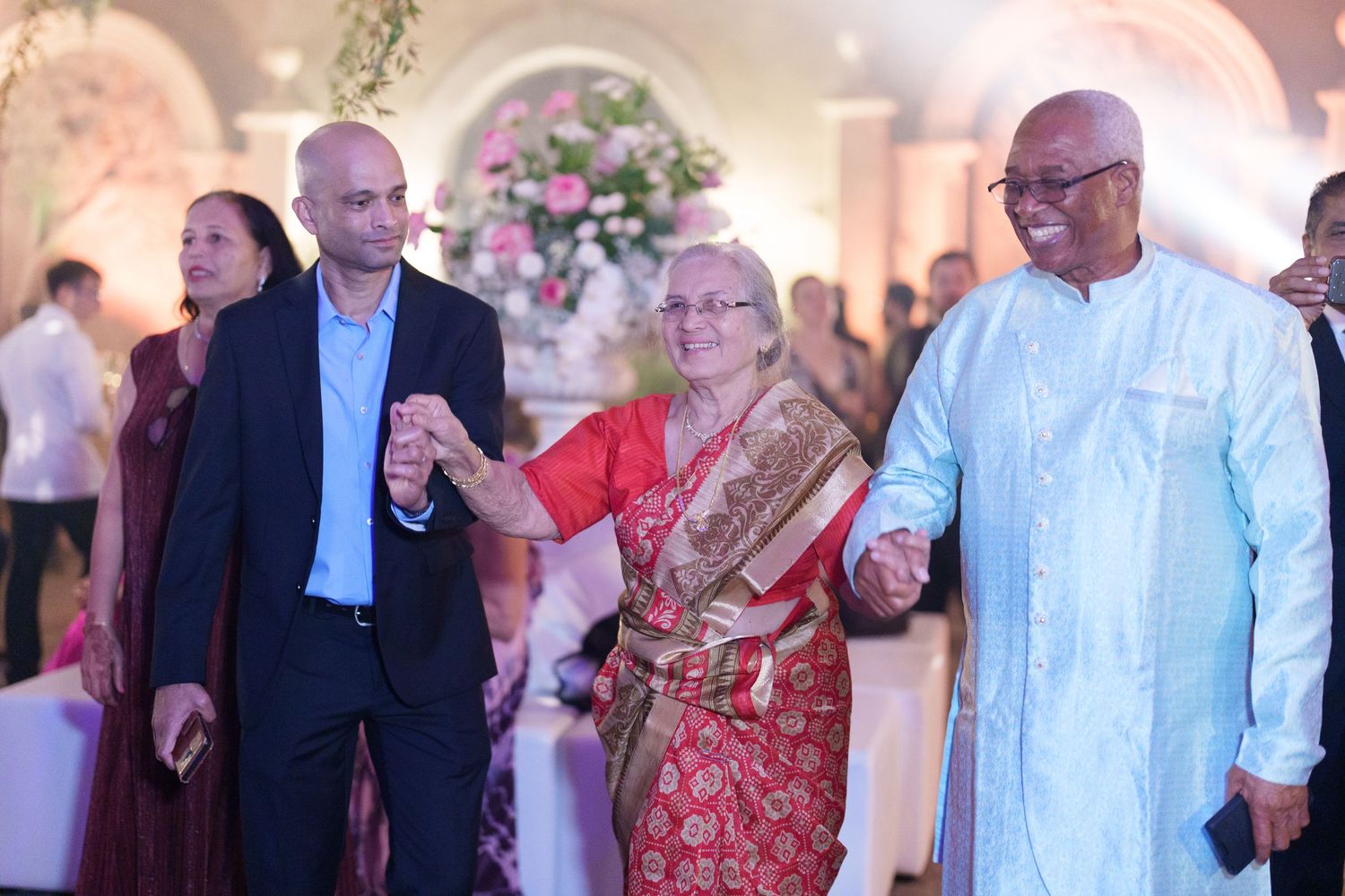 Formal wedding celebration with guests mingling in traditional attire under warm lighting.