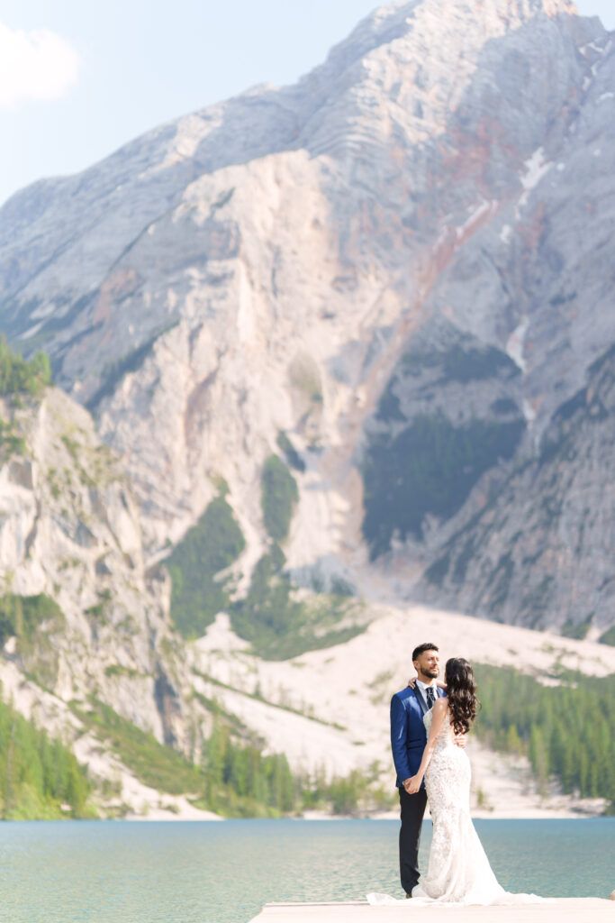 Wedding couple shares romantic moment by alpine lake with majestic mountain backdrop.