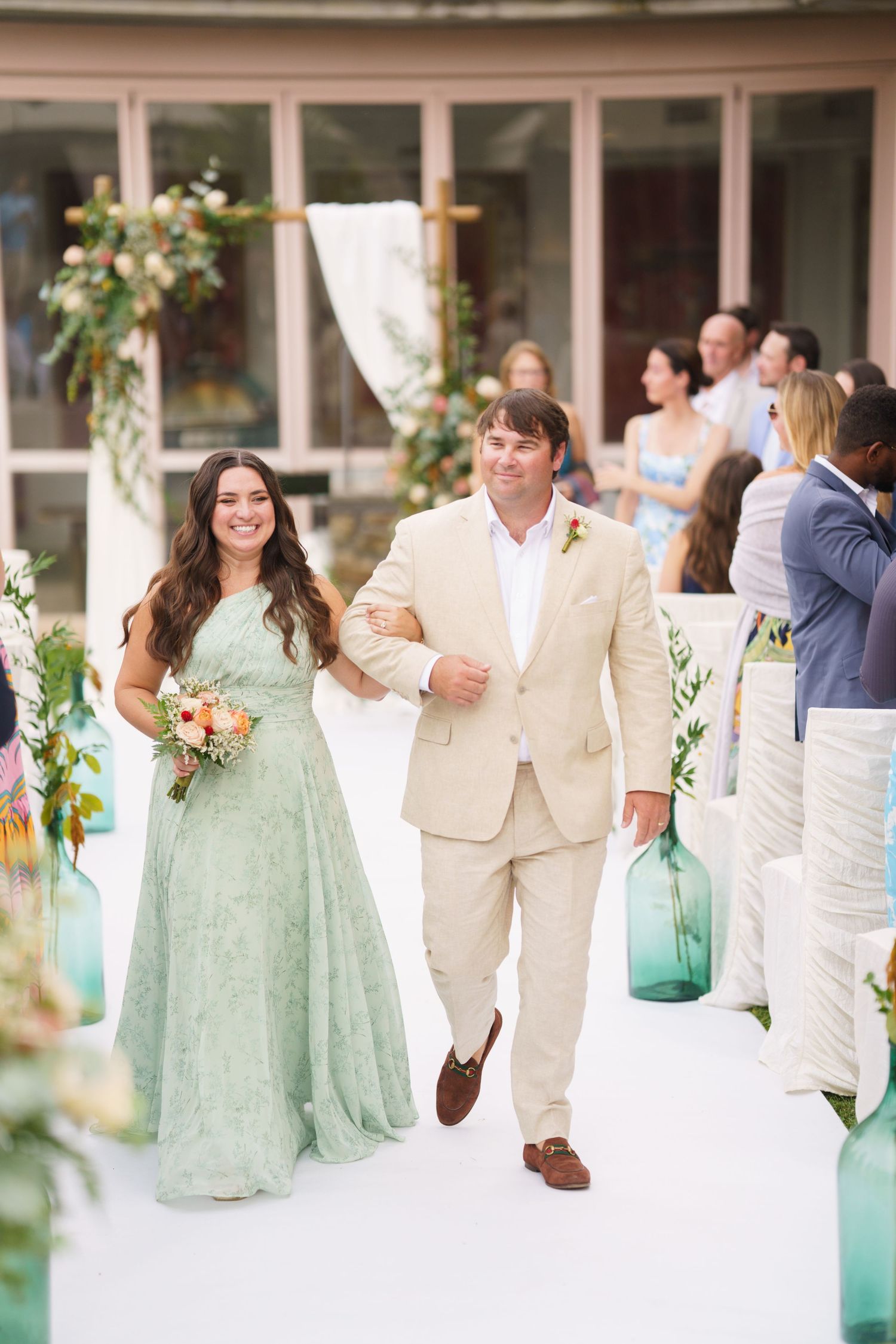 Wedding party members in mint green dresses and cream suits walk together at outdoor venue.