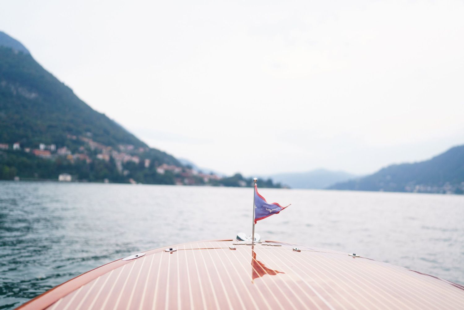A pink wooden dock extends into a scenic mountain lake surrounded by misty peaks and calm waters.
