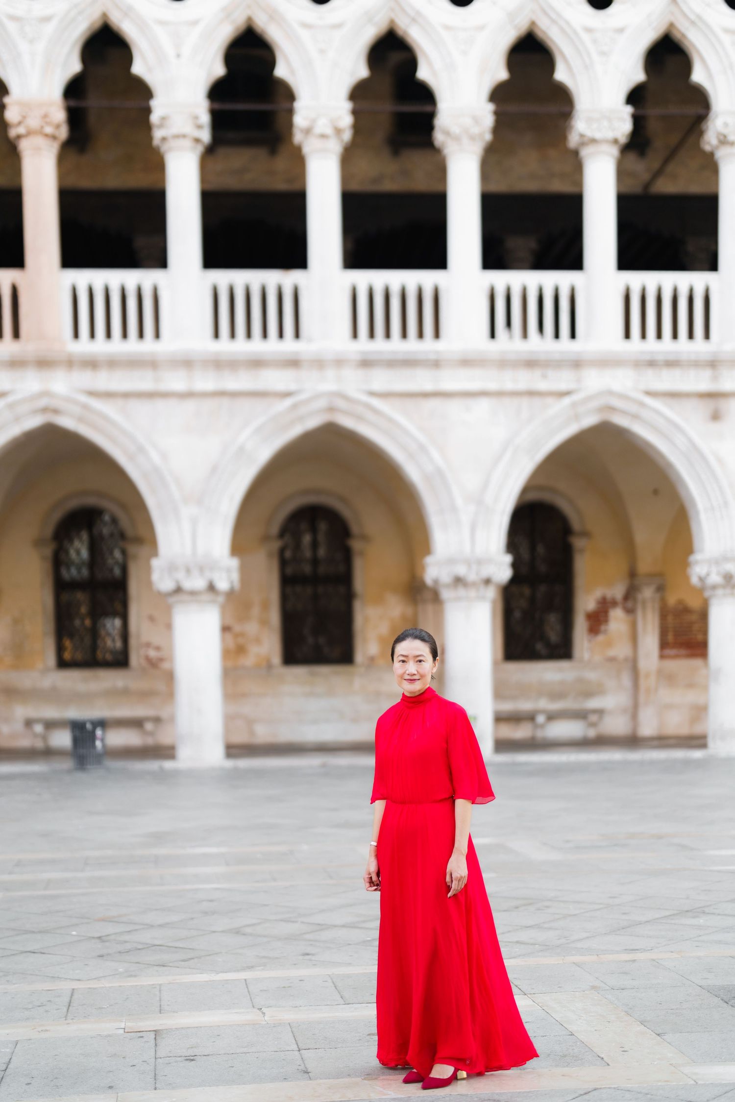 Woman in red dress posing in front of Doge's Palace Gothic arches in Venice, Italy.