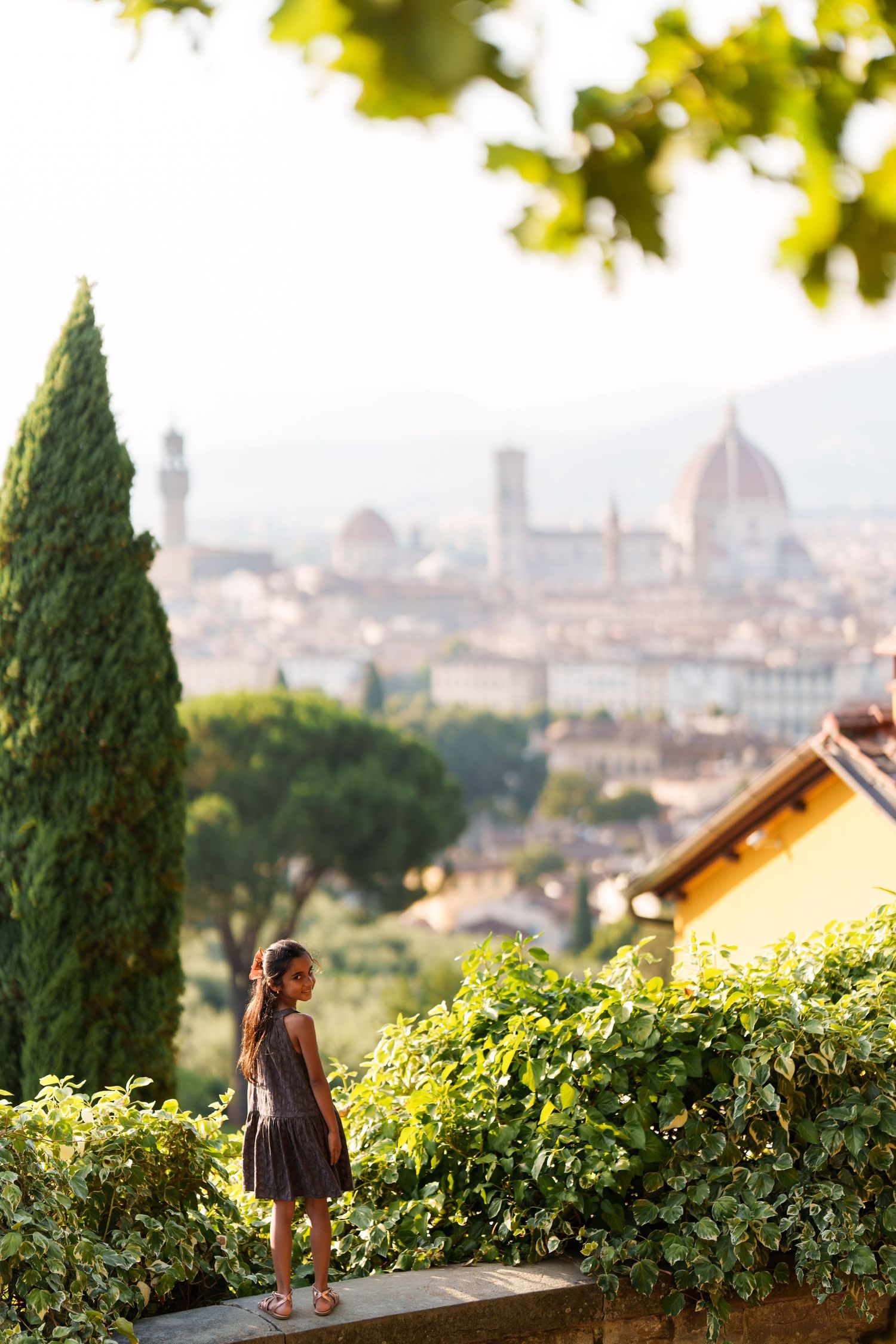 A young girl in a gray dress stands on a wall overlooking the Florence skyline with the Duomo cathedral in the background.