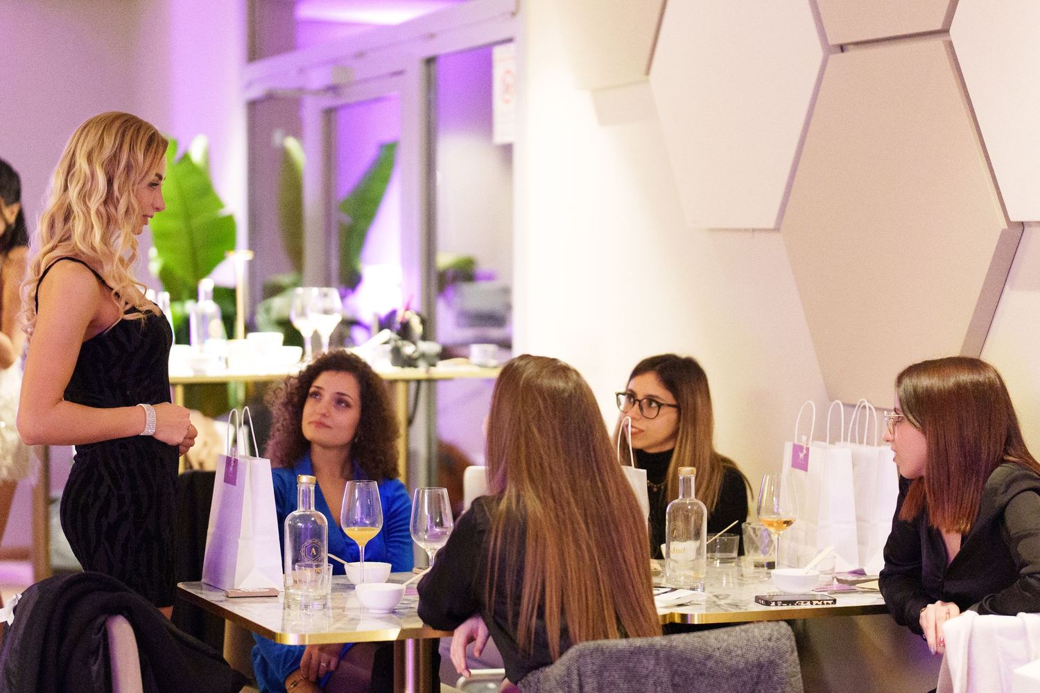 Women networking at an elegant dinner event, seated around a table with wine glasses in a modern venue.