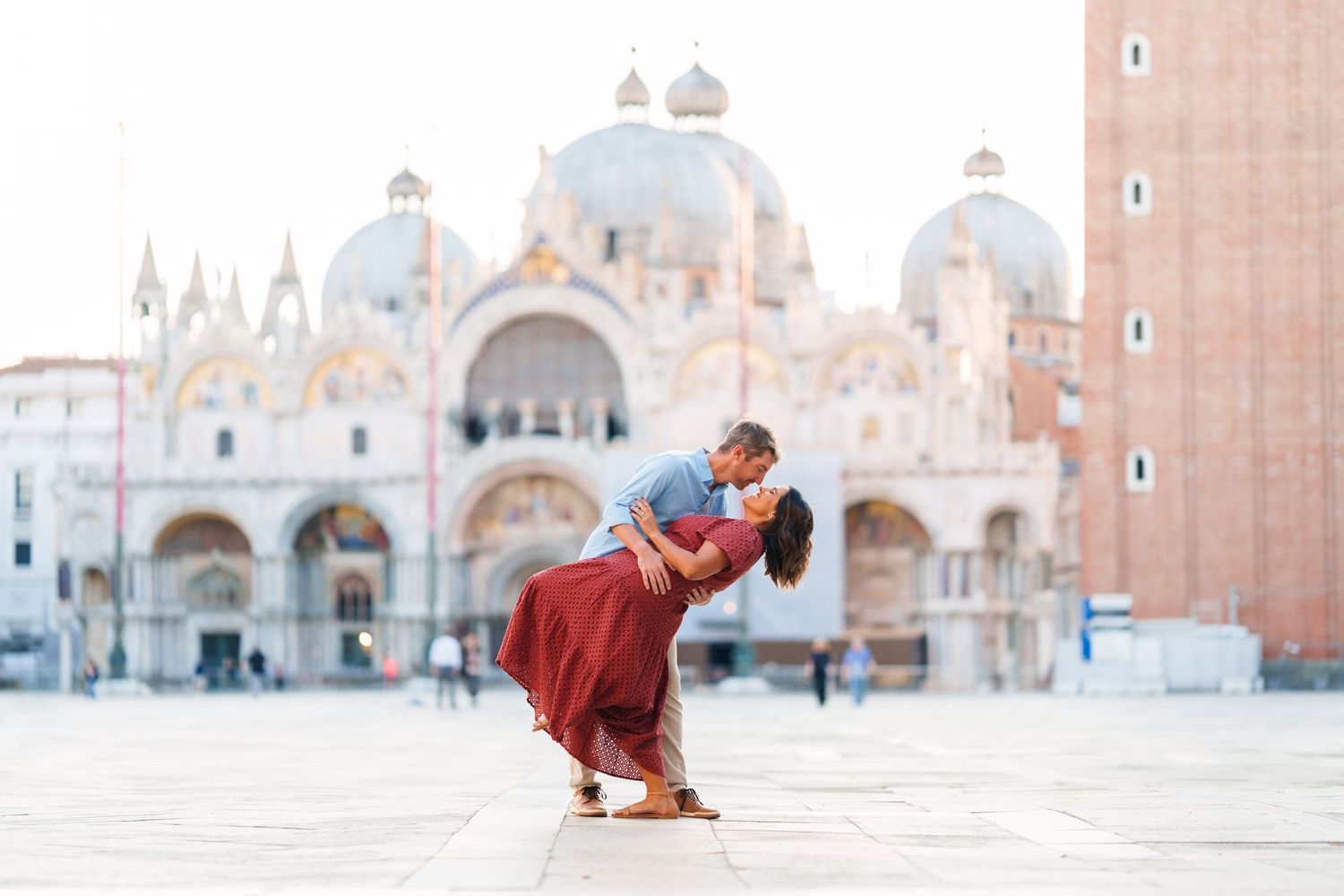 Couple sharing a romantic dip kiss in St. Mark's Square, Venice, with the iconic Basilica in the background.