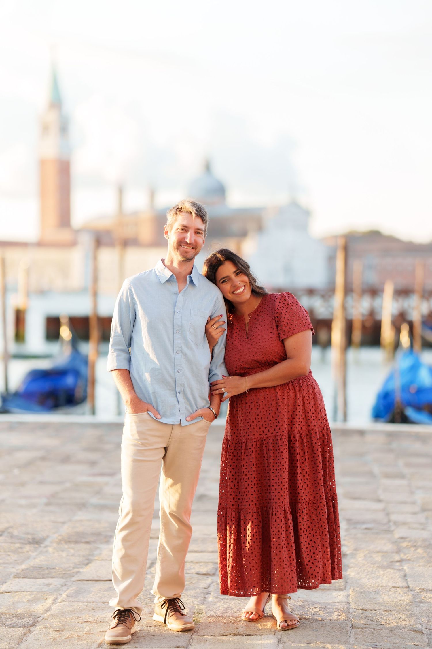 Couple posing together on a Venice waterfront promenade with gondolas and San Giorgio Maggiore church in the background.