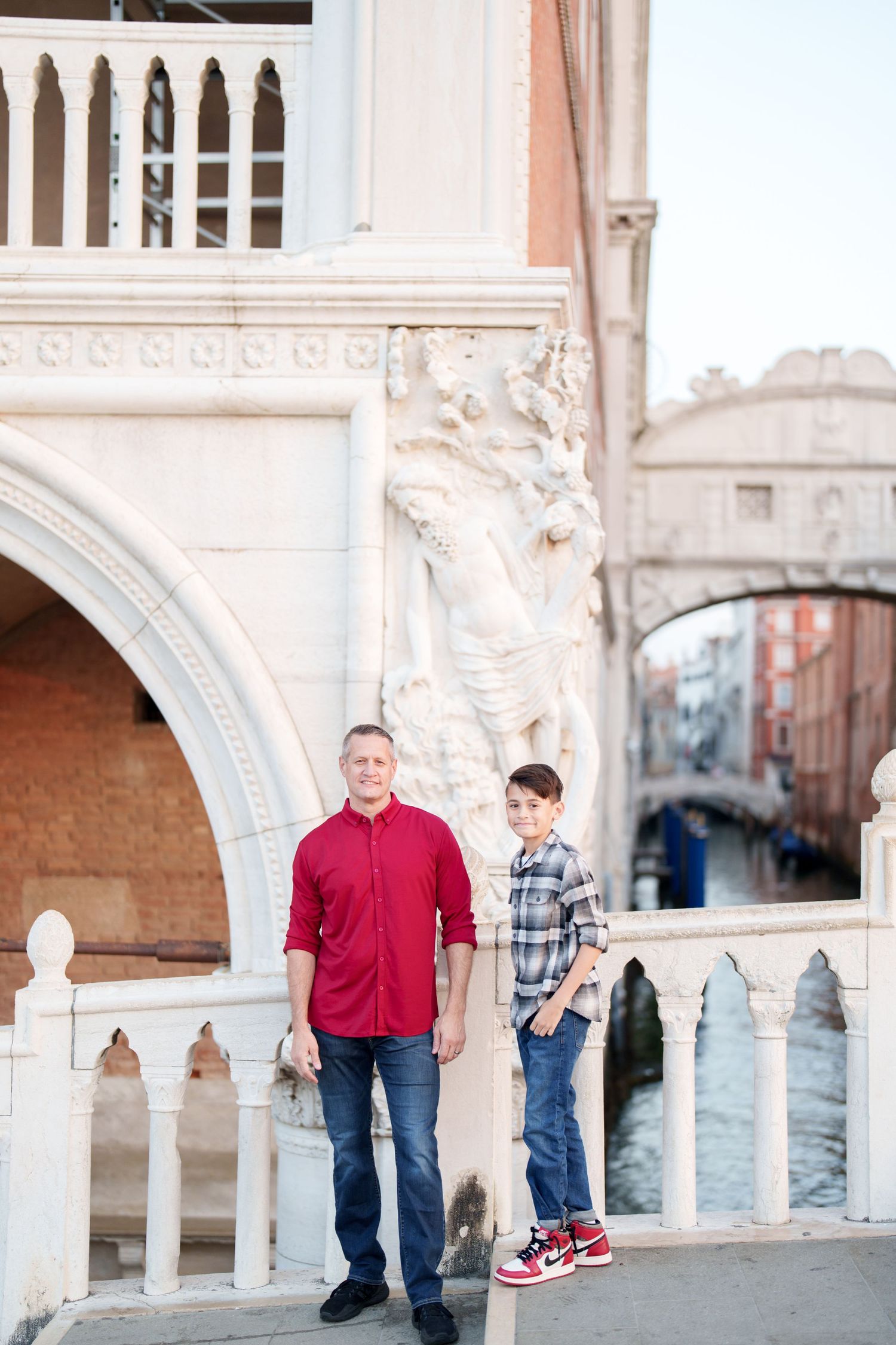 Two people stand by ornate Venetian architecture near the Bridge of Sighs and a canal in Venice, Italy.
