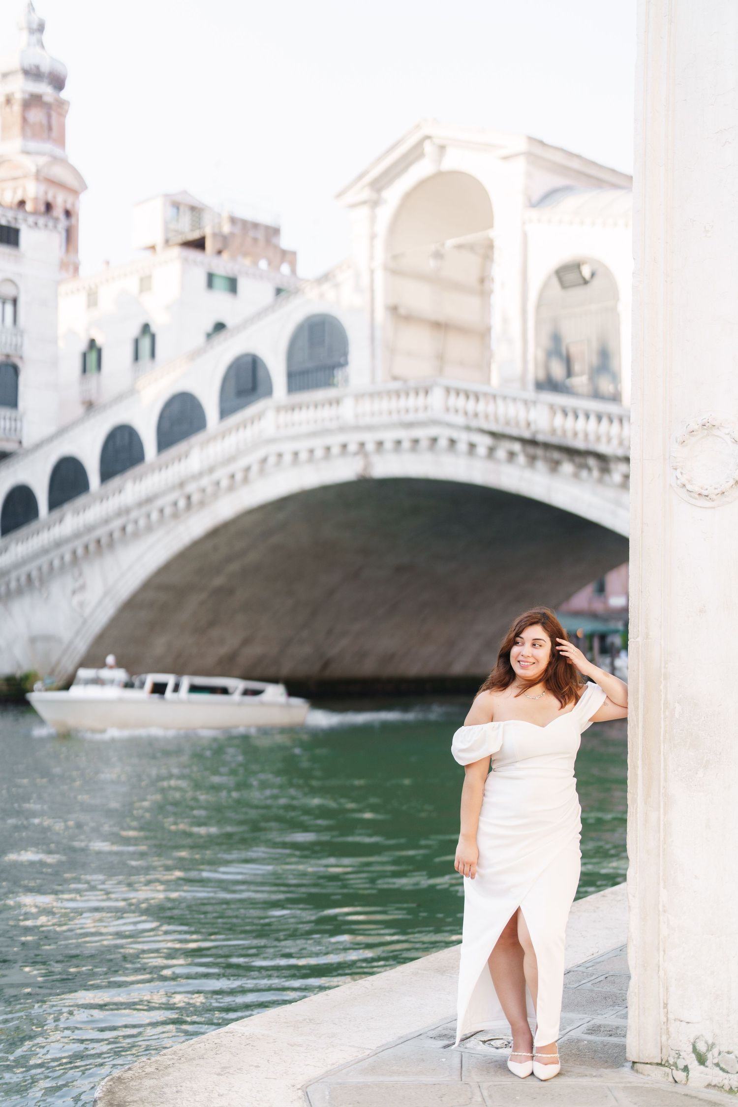 A white dress against the iconic Rialto Bridge in Venice, Italy with turquoise canal waters in the background.