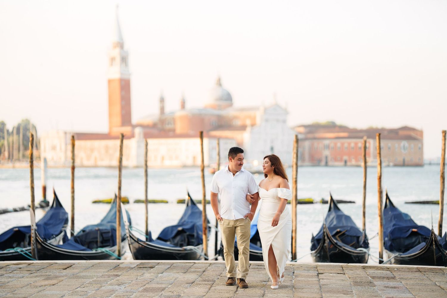 Romantic couple embraces in front of gondolas and San Giorgio Maggiore church in Venice, Italy during sunset.