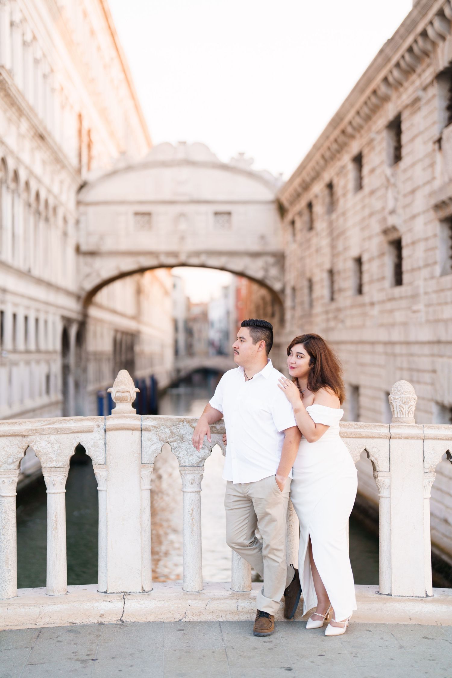 A romantic couple in white outfits poses along the historic Bridge of Sighs in Venice, Italy.