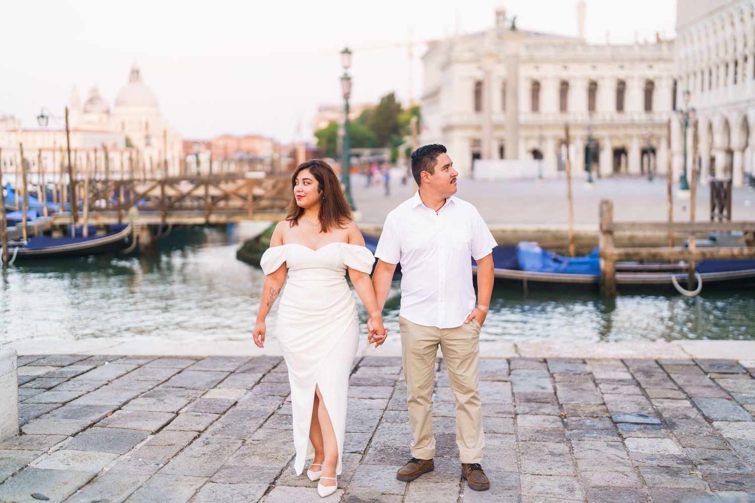 A romantic couple strolls along the cobblestone streets and canals of Venice, Italy wearing coordinated white outfits.