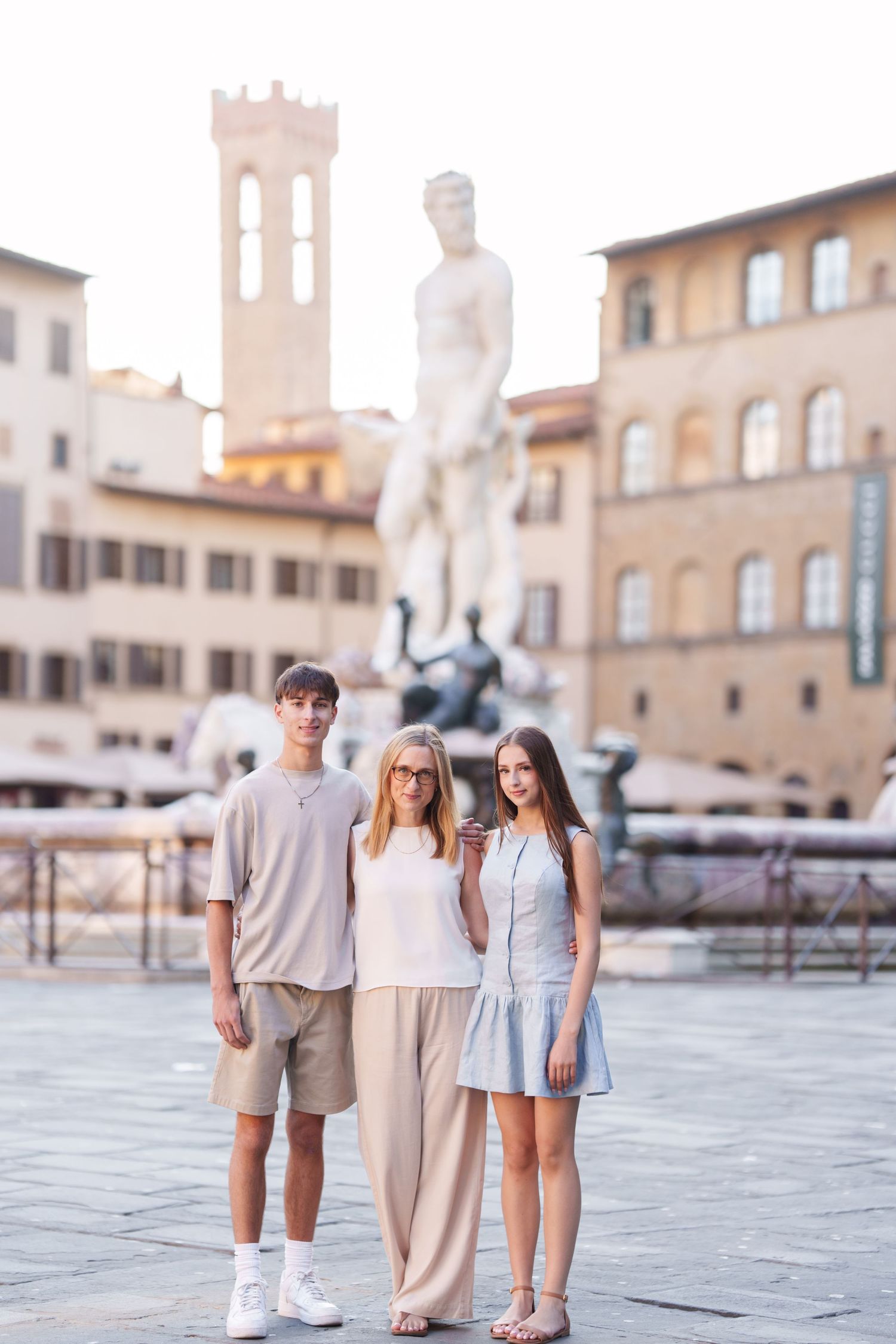 photographer Florence Family wearing coordinated neutral outfits poses together in historic Italian plaza with stone buildings and statues.