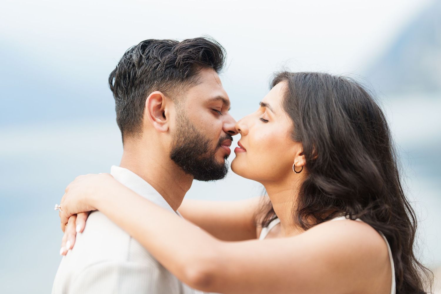 A romantic couple shares a tender kiss against a soft blurred background.