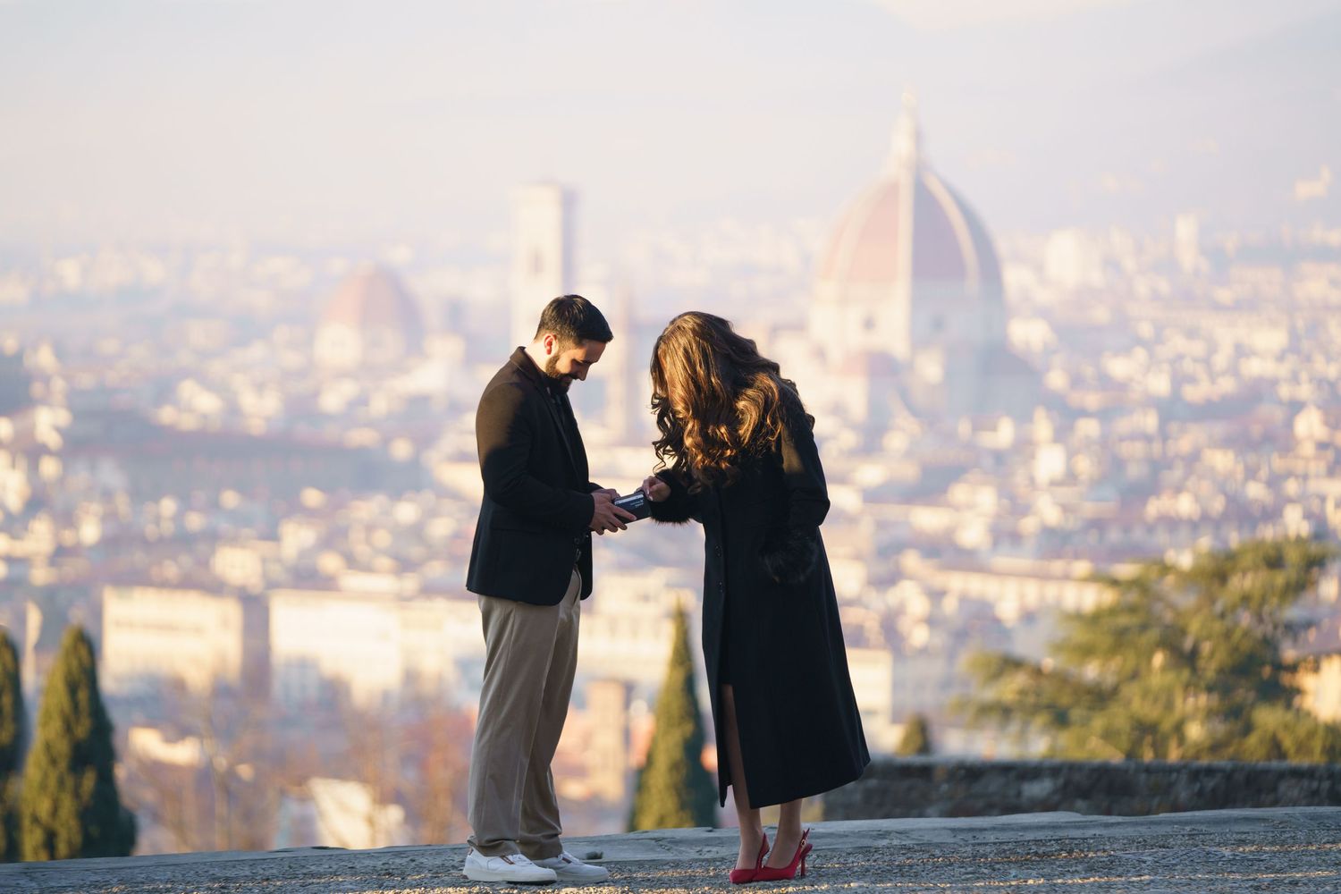 A couple shares a romantic moment at sunset overlooking a scenic cityscape from an elevated viewpoint.