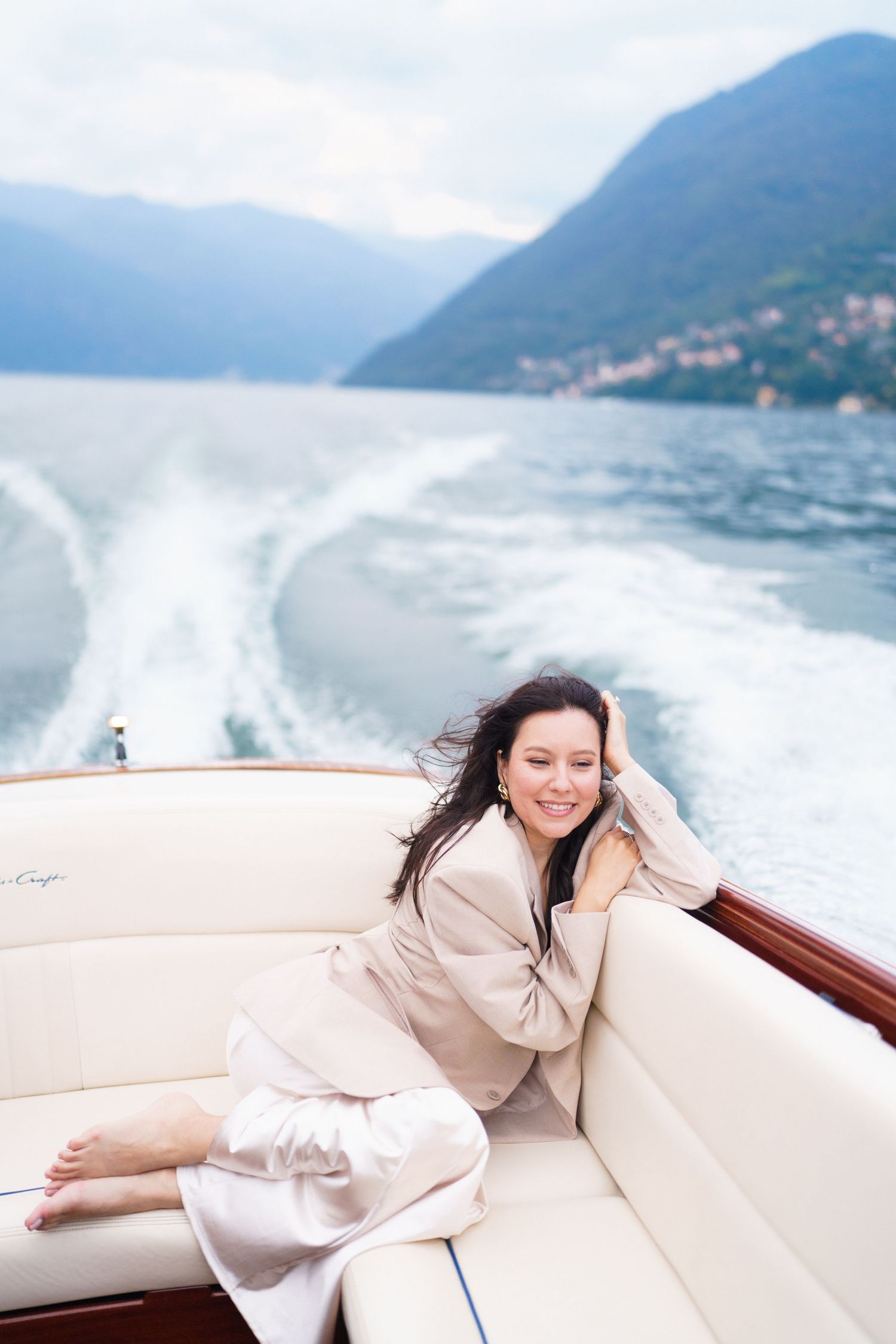 Someone relaxes on cushioned seating of a luxury boat while cruising past mountains on a scenic lake.