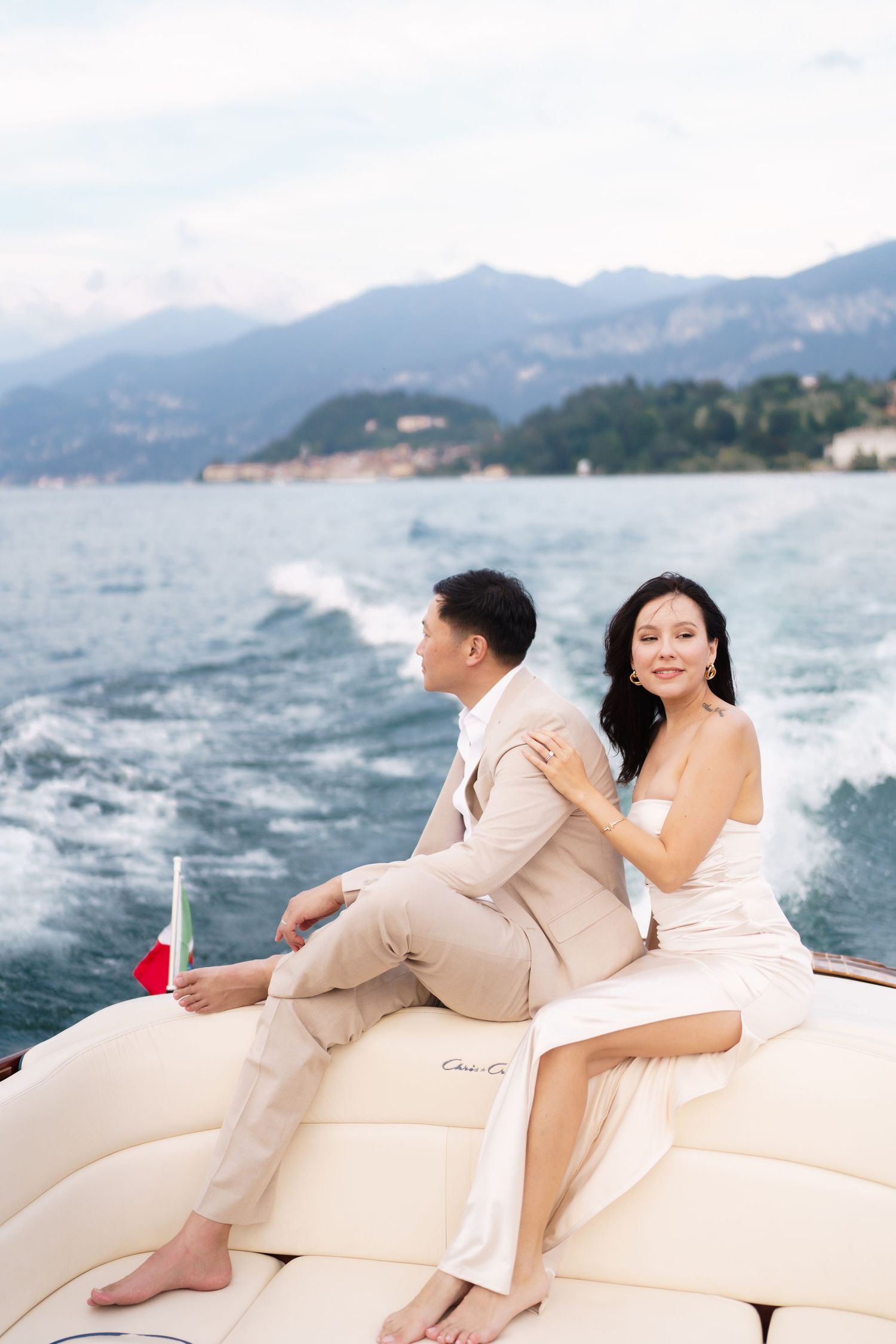 Couple relaxing on luxury yacht cushions with mountains and ocean waves in background.