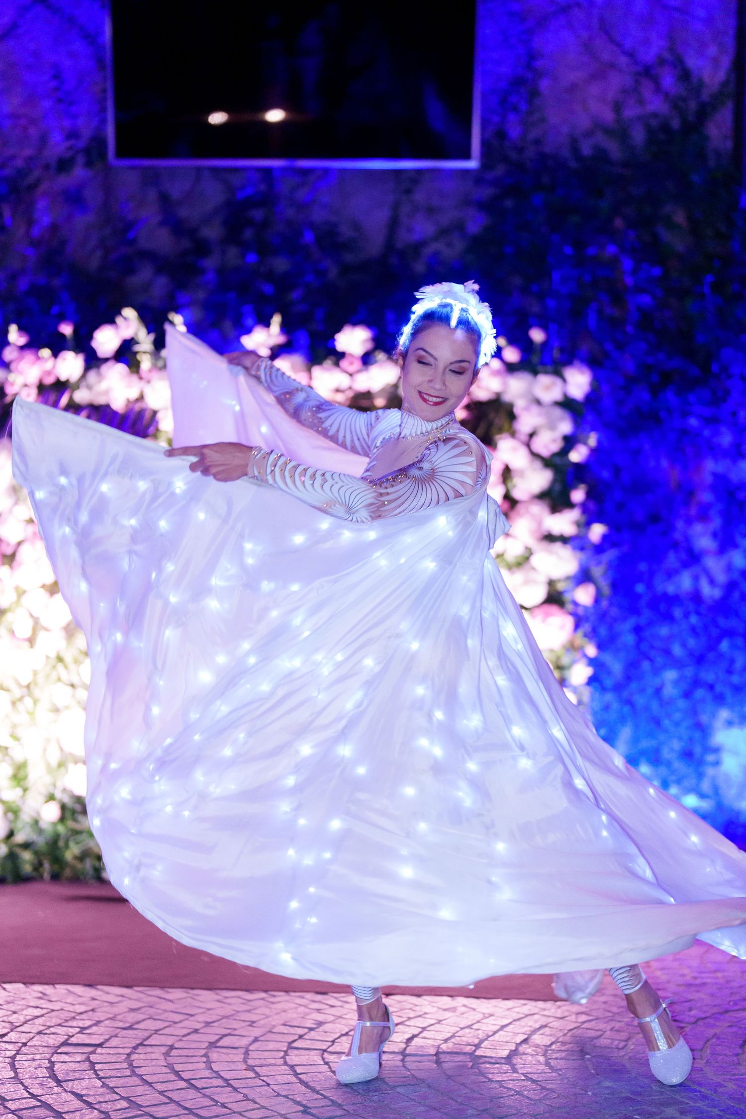 Illuminated white dress spinning on dance floor against deep blue atmospheric lighting.