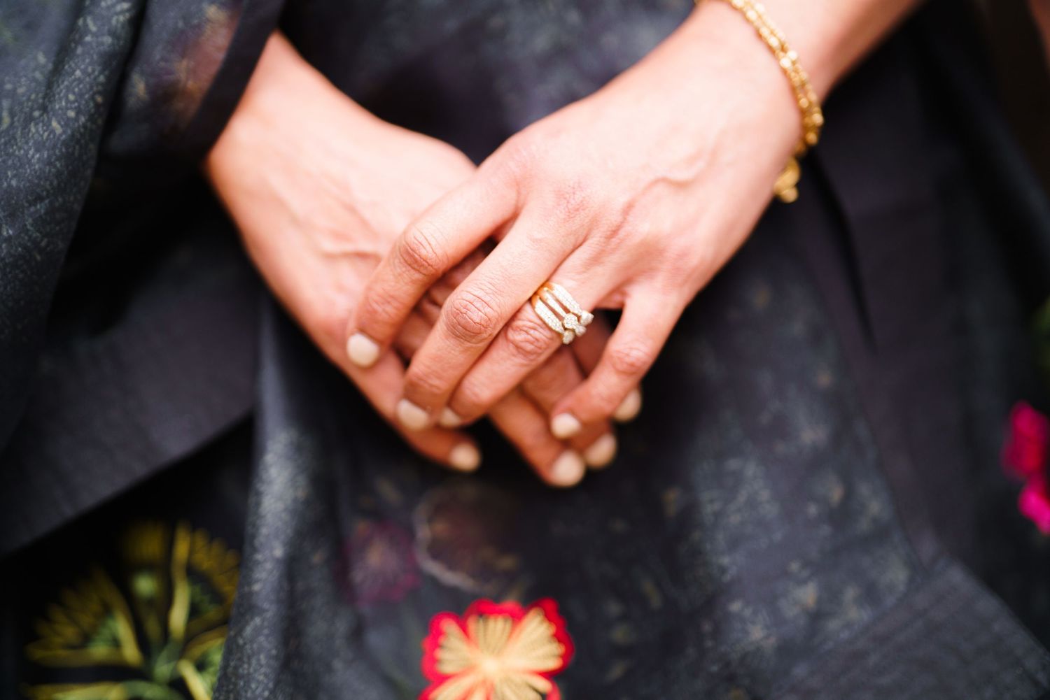 Close-up of hands showing jewelry and rings against dark fabric.
