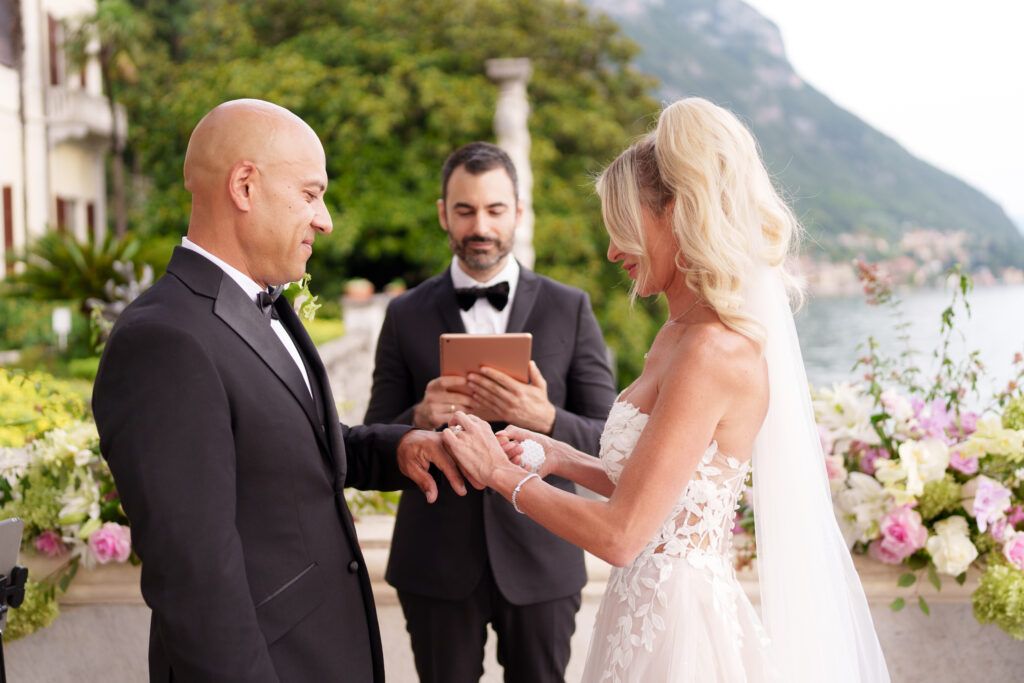 Wedding ceremony exchange on a flower-decorated terrace with lake and mountain views.
