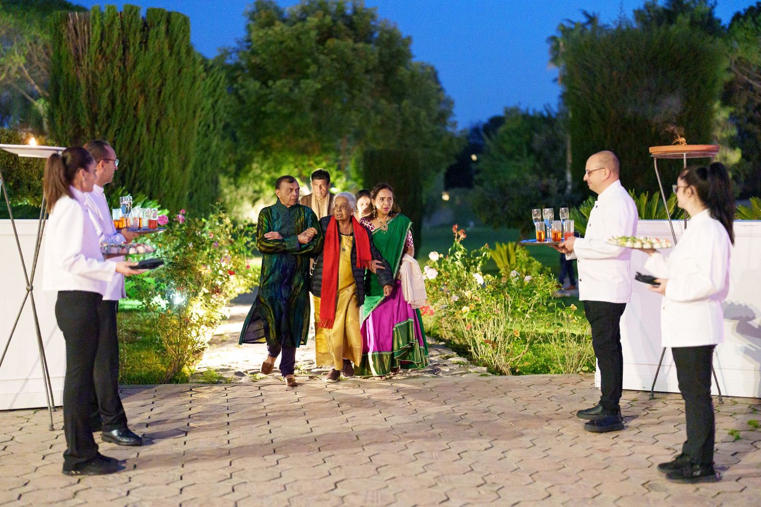 Garden party setup with illuminated pathways and guests mingling in formal attire.