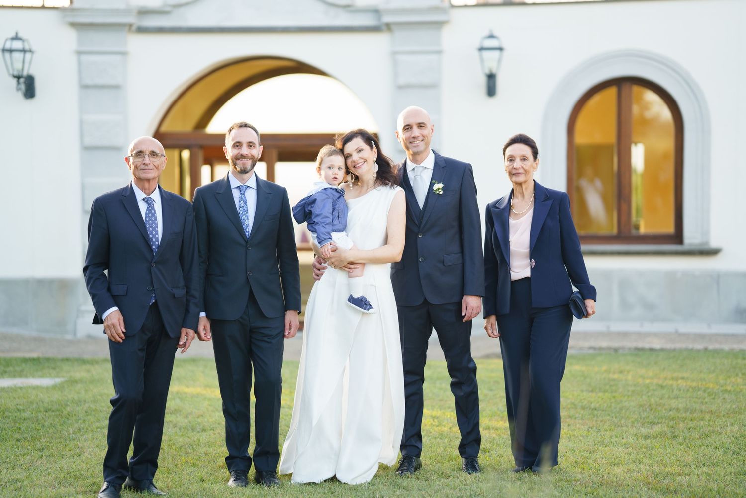 Wedding party group photo in front of white stucco building with arched doorways.