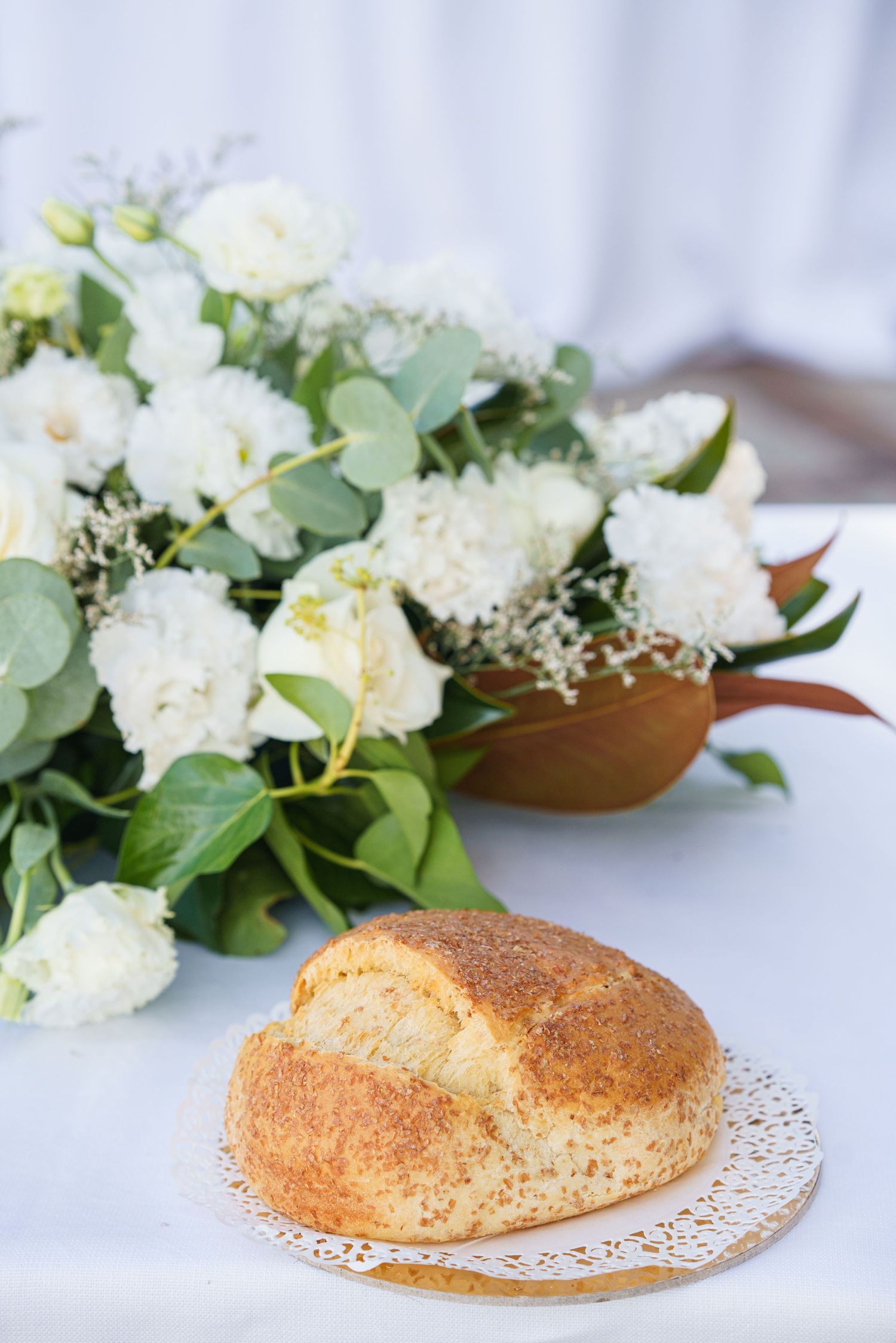 White floral arrangements with fresh bread on lace doilies for wedding table settings.