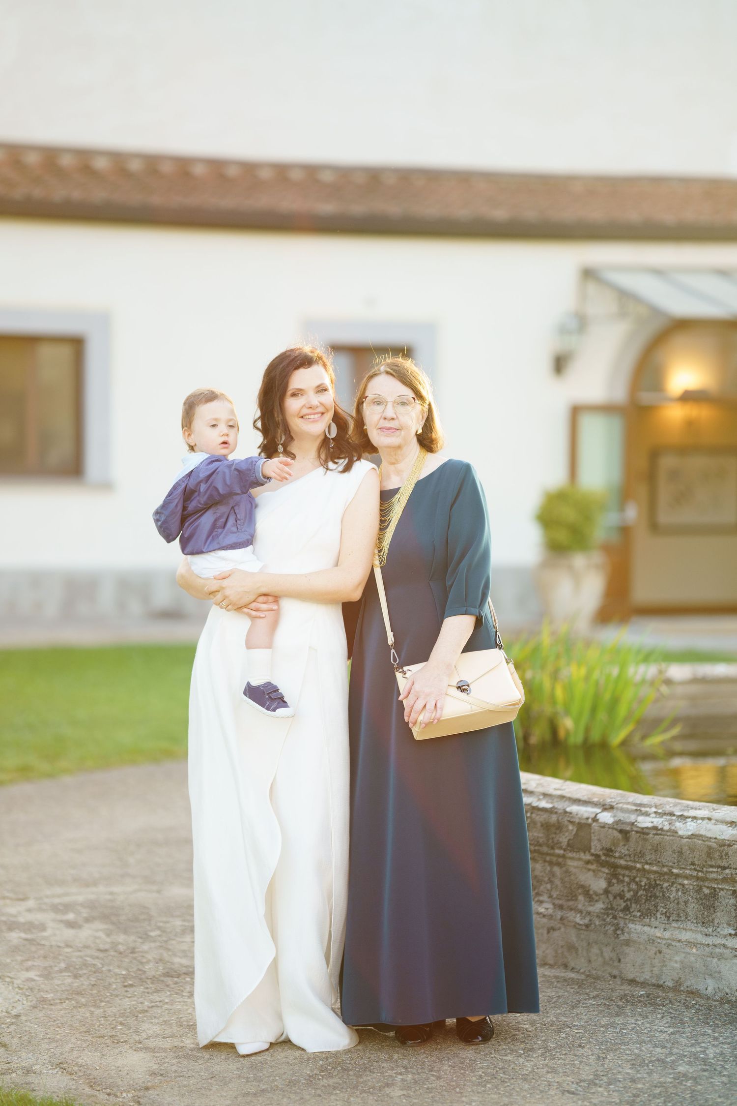 Three people pose together in formal wear outside building during evening celebration.