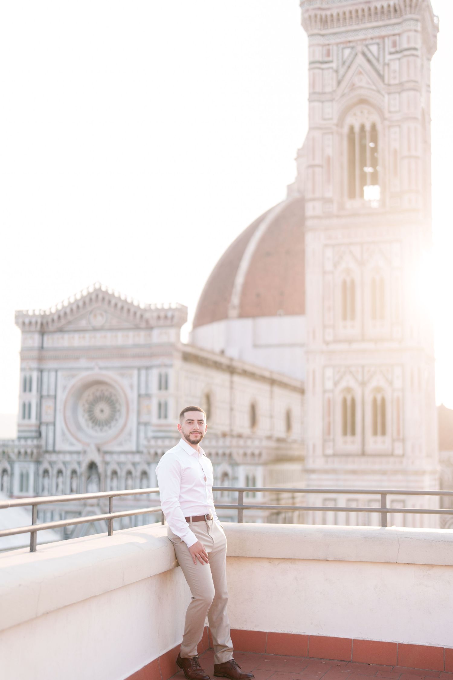 A person in light clothing poses on a rooftop terrace overlooking Florence Cathedral during golden hour.
