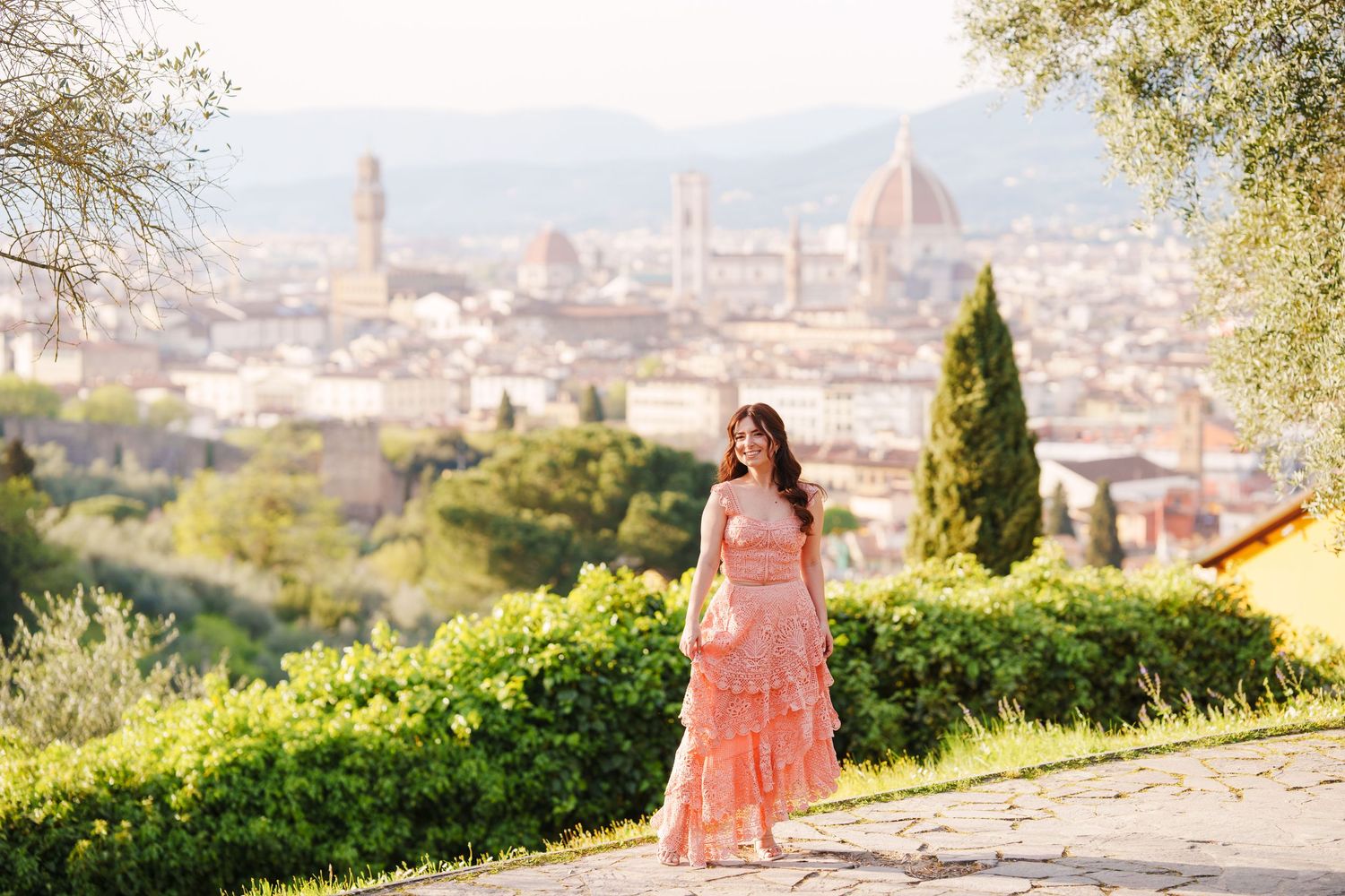 A scenic overlook in Florence, Italy with the iconic Duomo cathedral dome visible in the distance among cypress trees and gardens.