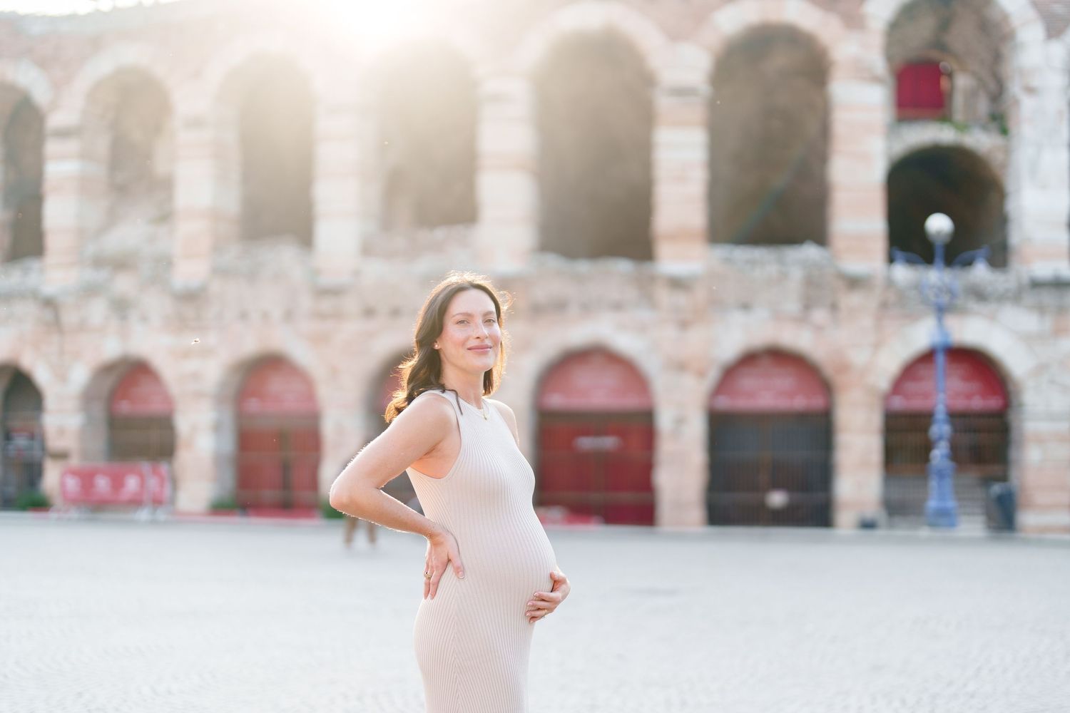 Verona photographer A person in a white dress twirls gracefully in front of an ancient stone building with arched columns.