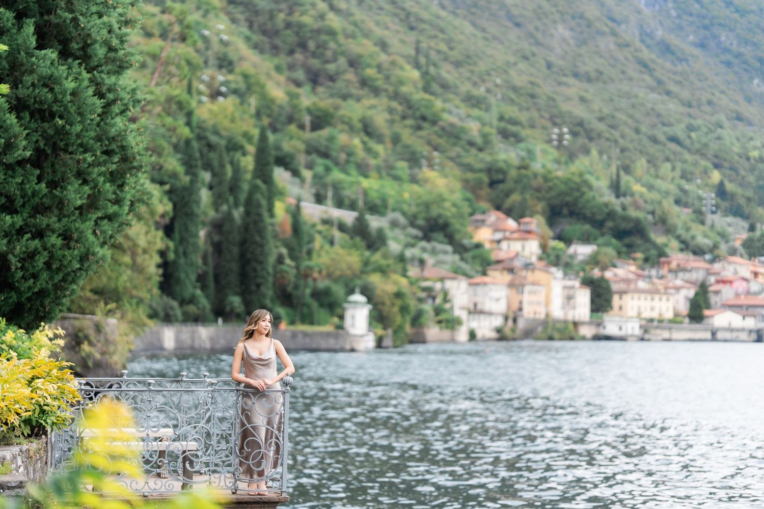 People cycling along scenic Lake Como in Italy with mountains and waterfront buildings in the background.
