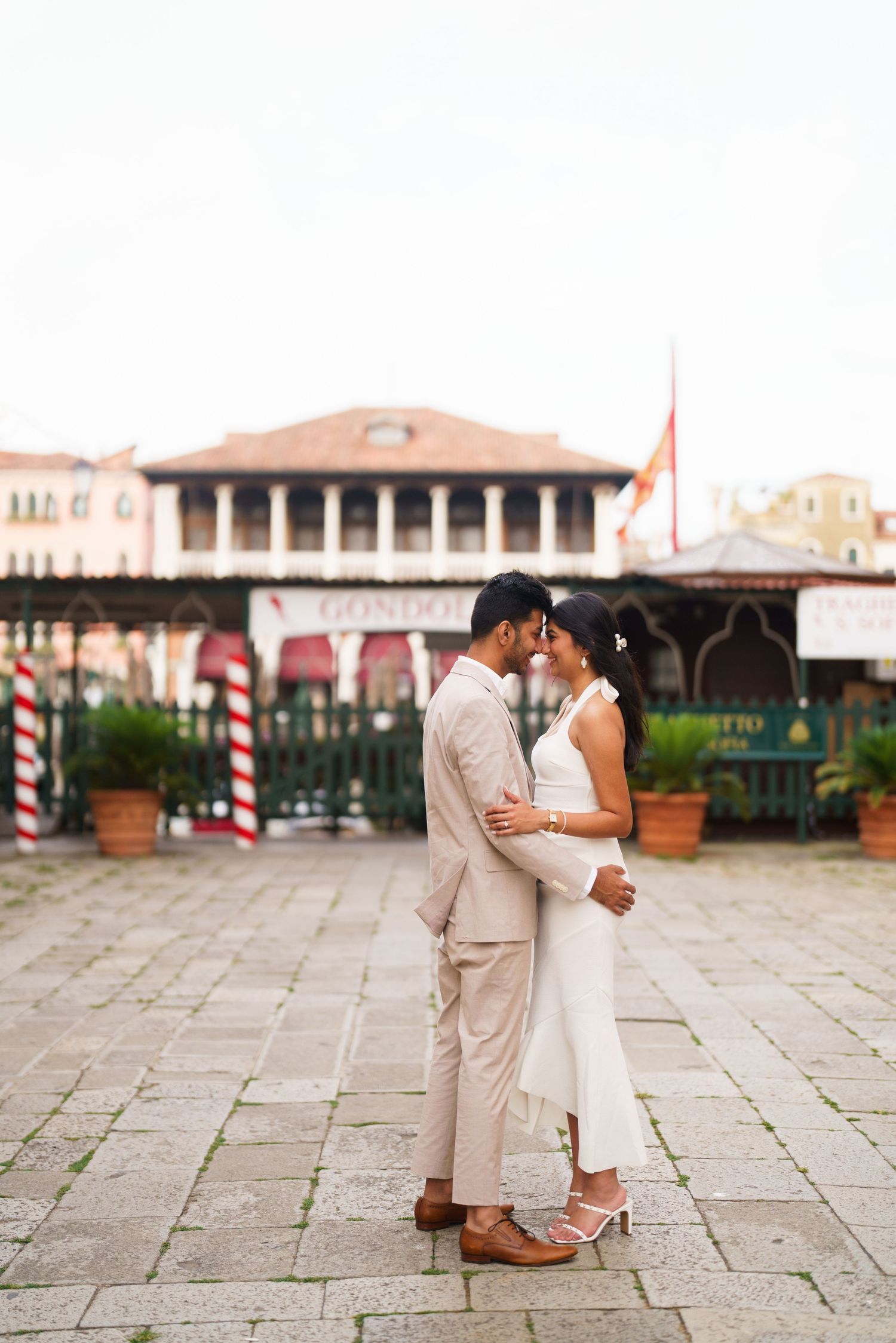A romantic couple in beige and white attire share intimate moments in a series of photos on a stone plaza.