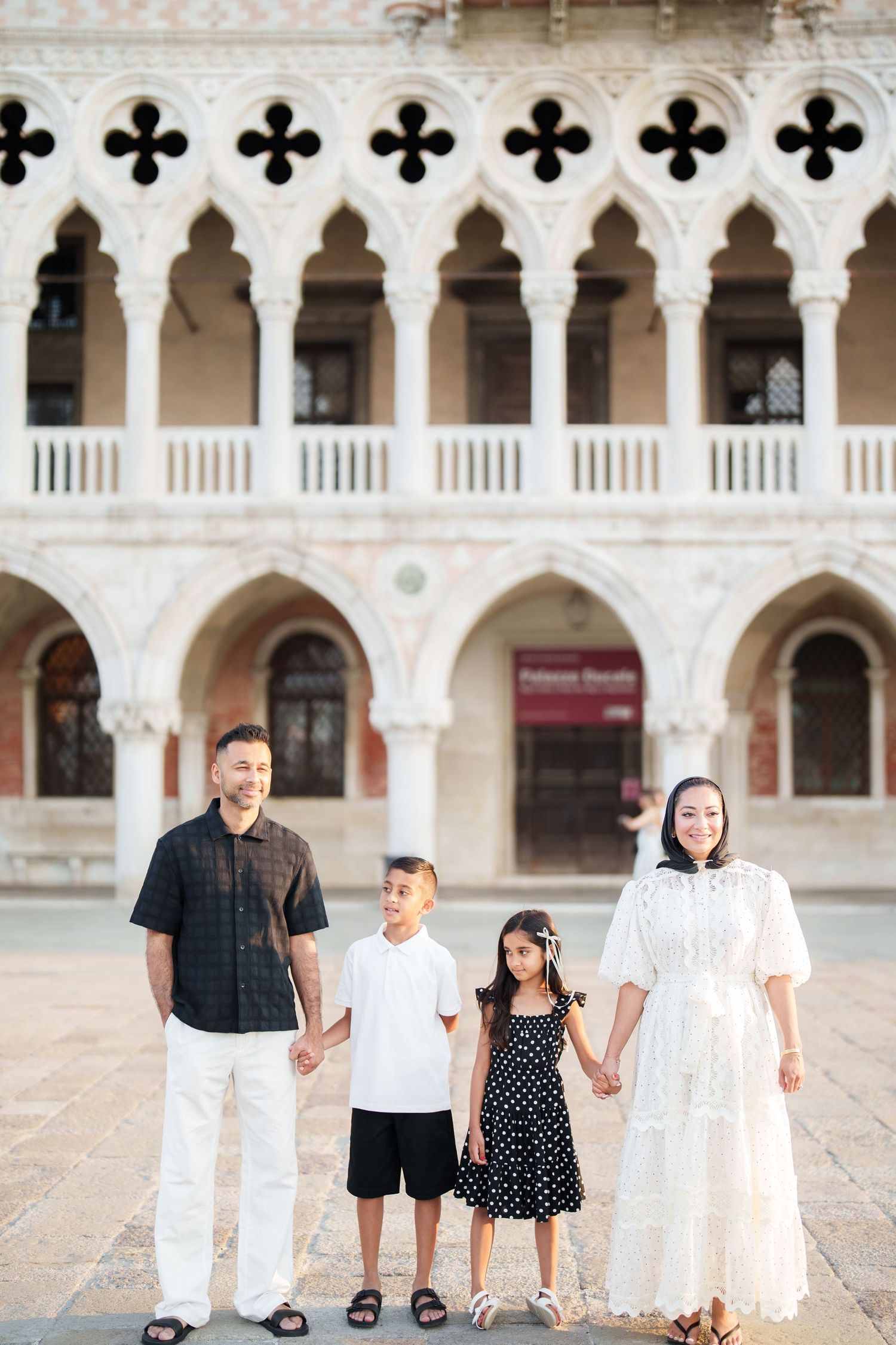 Family of four holding hands in front of the ornate Palazzo Ducale in Venice, Italy.